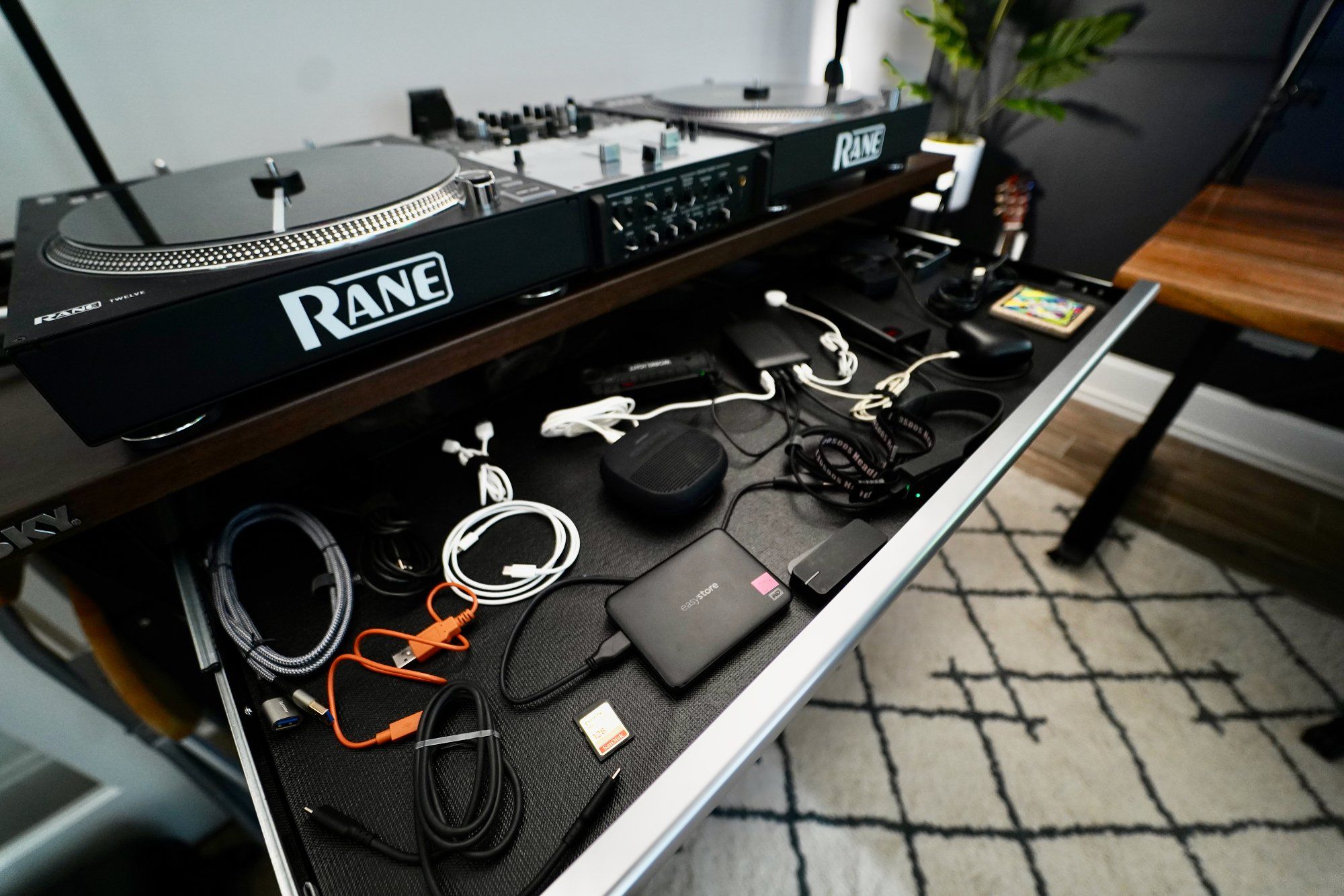 A DJ setup workbench with a thin sliding drawer that doubles as a home charging station and storage for peripherals