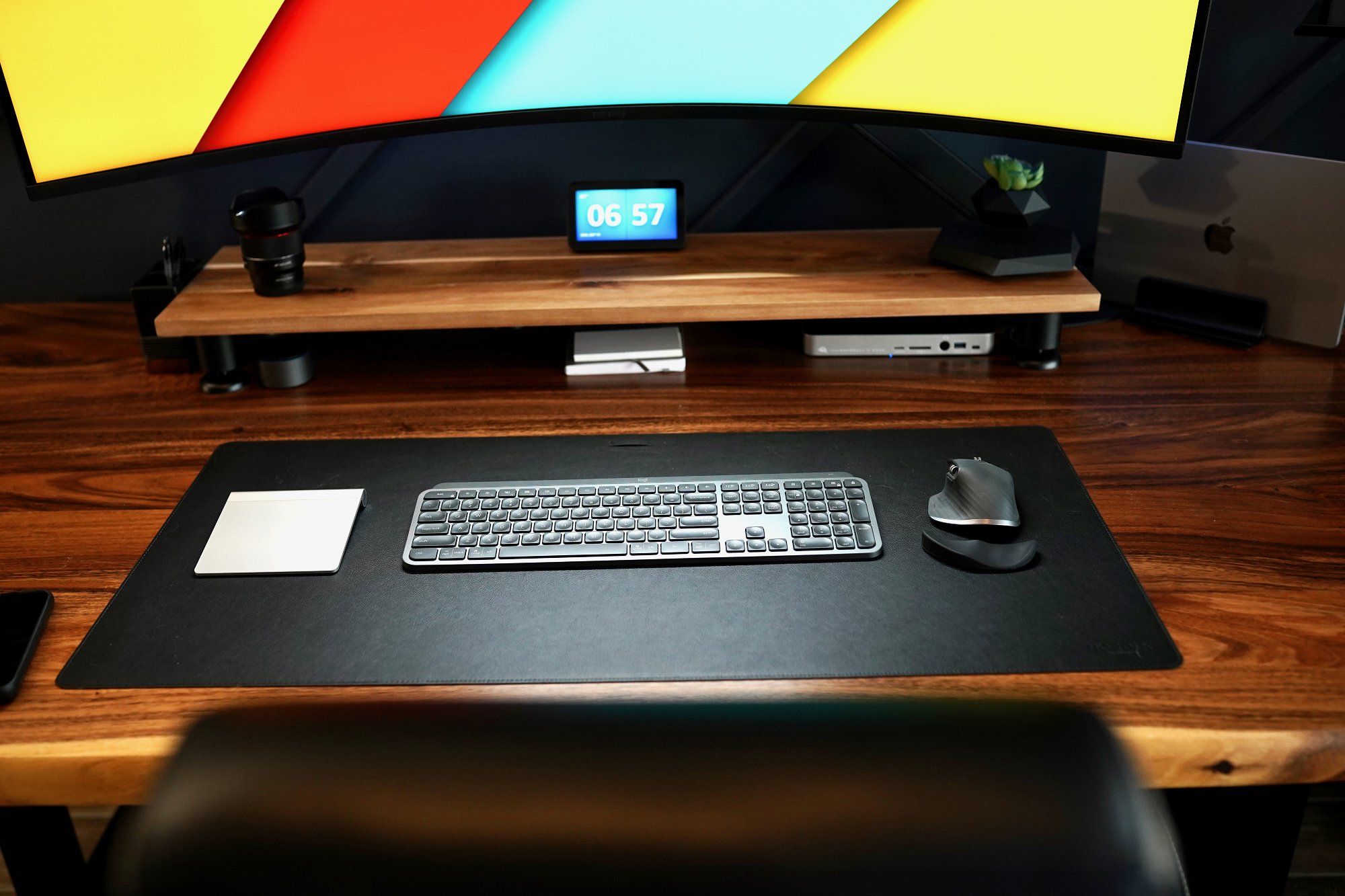 An Apple Magic Trackpad, a Logitech MX keyboard, and a Logitech MX Master 3 mouse lying on the desk mat in a home office