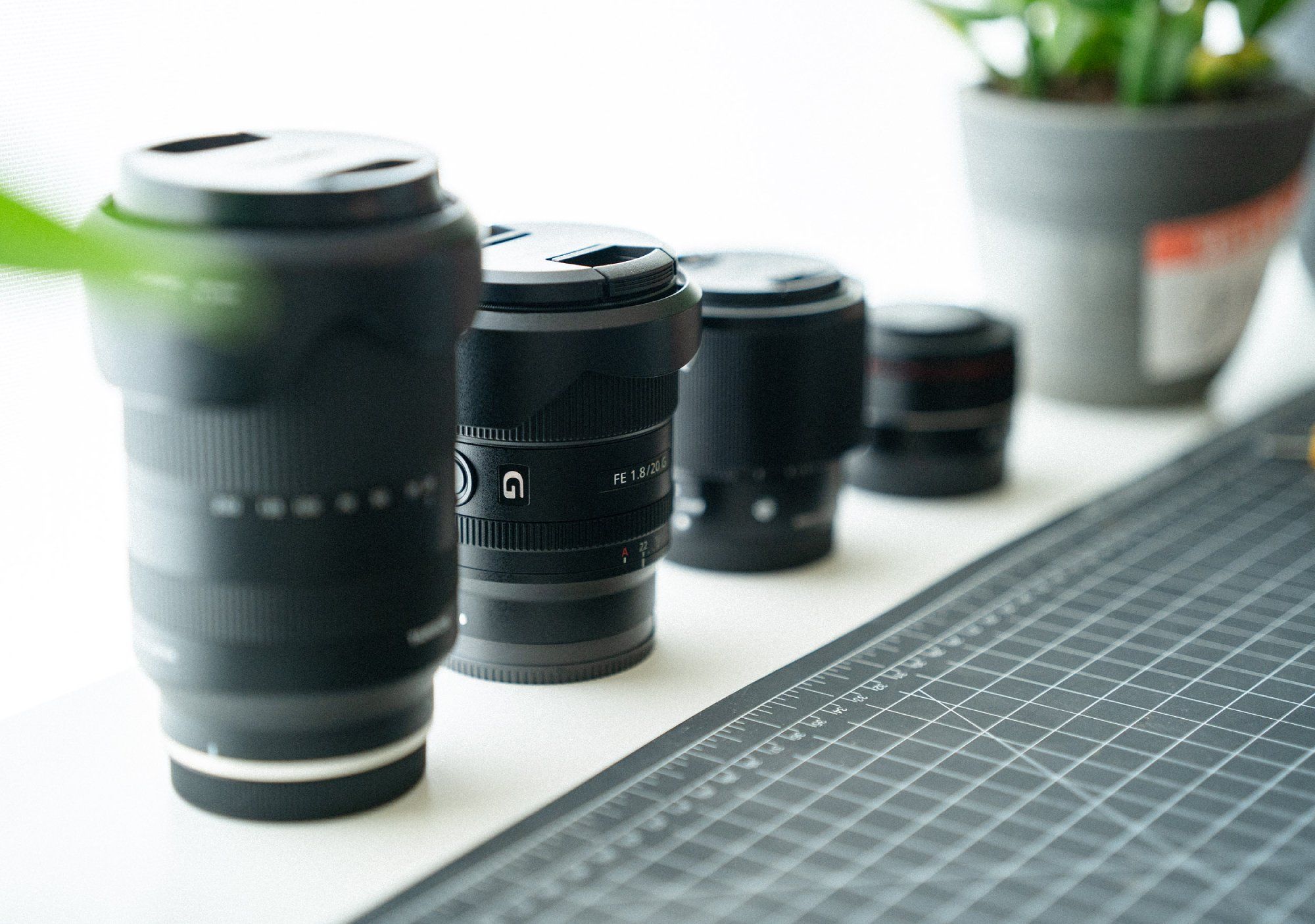 Four camera lenses, a cutting mat, and an indoor plant in the background