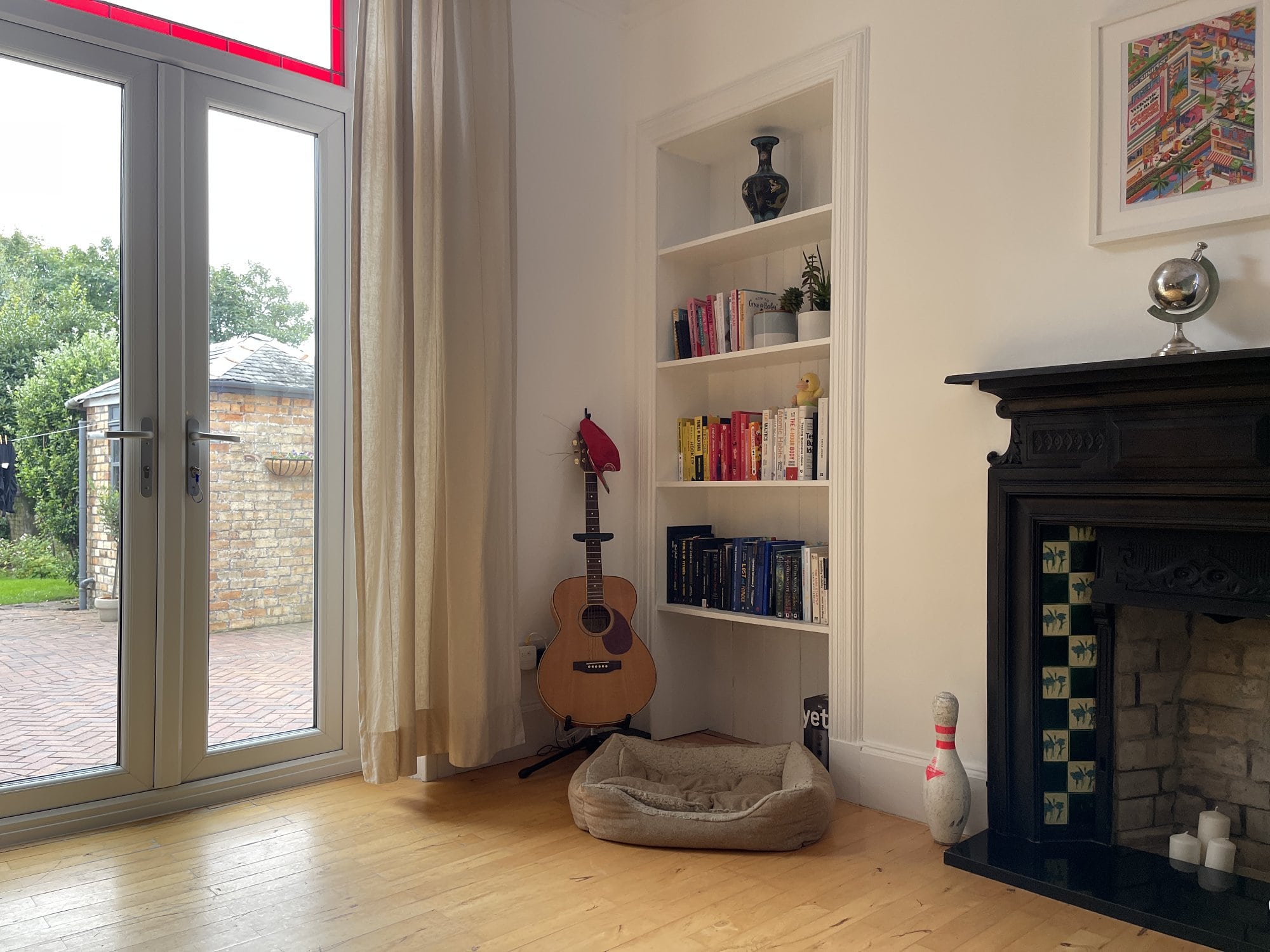 A room that features a fireplace, a guitar propped on a stand, a dog bed, and shelves adorned with books