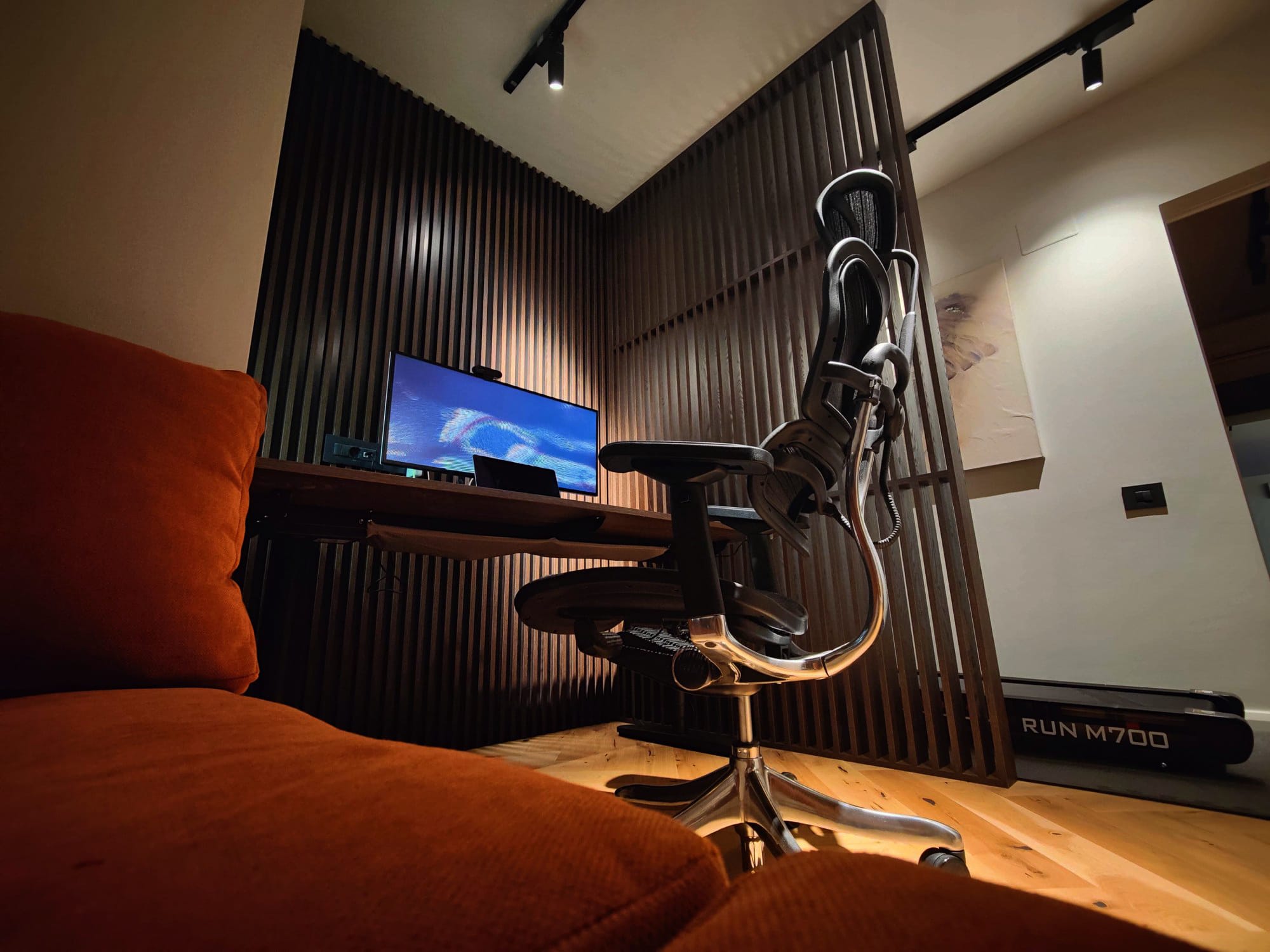A stylish slatted wall home office setup with an ergonomic office chair in the foreground, a desk with a monitor displaying an abstract scene, and ambient lighting creating a warm and inviting atmosphere
