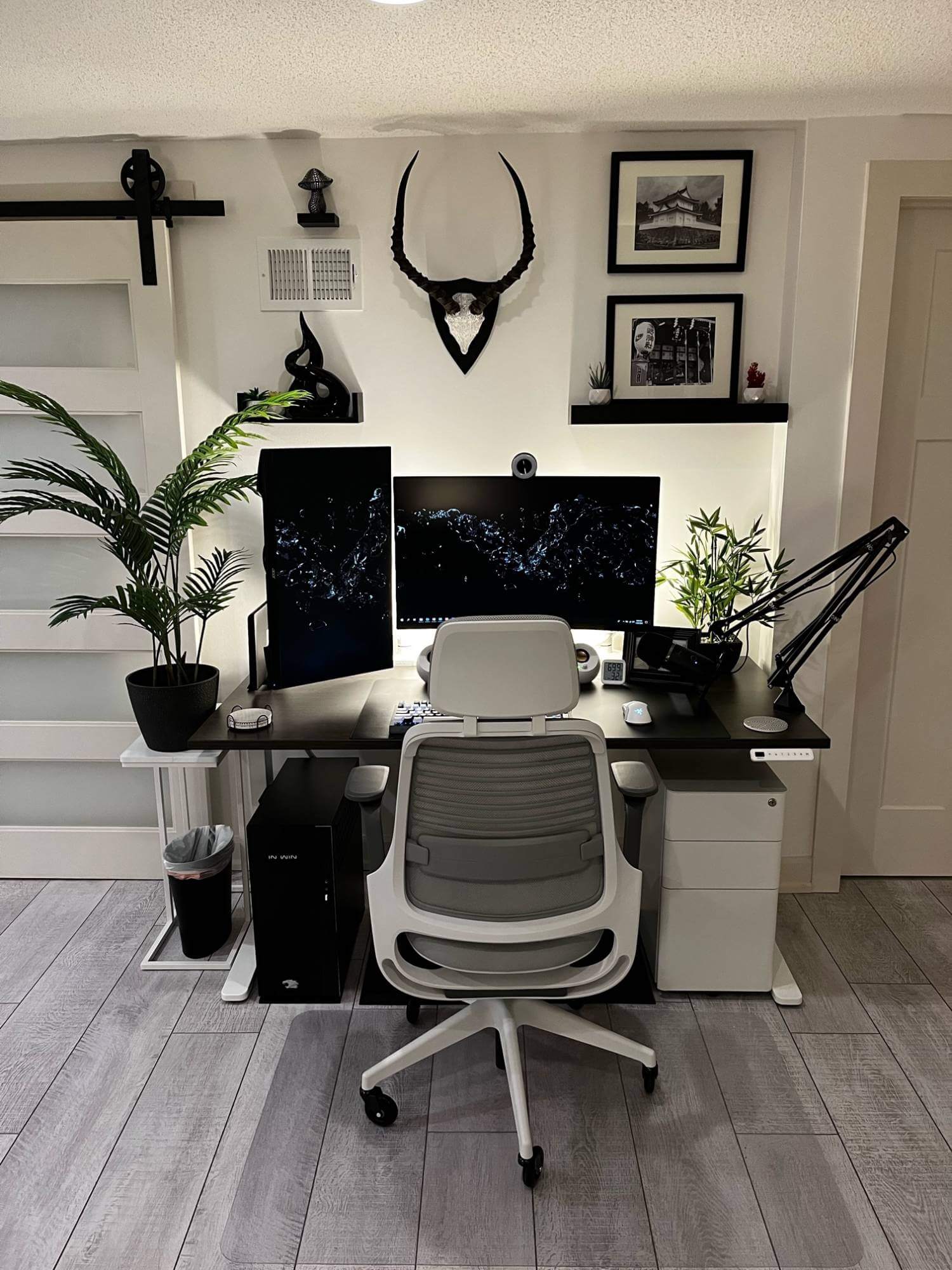 A minimalist dual-monitor workspace with an ergonomic chair, decorative plants, and framed artwork, all neatly arranged in a bright, contemporary room