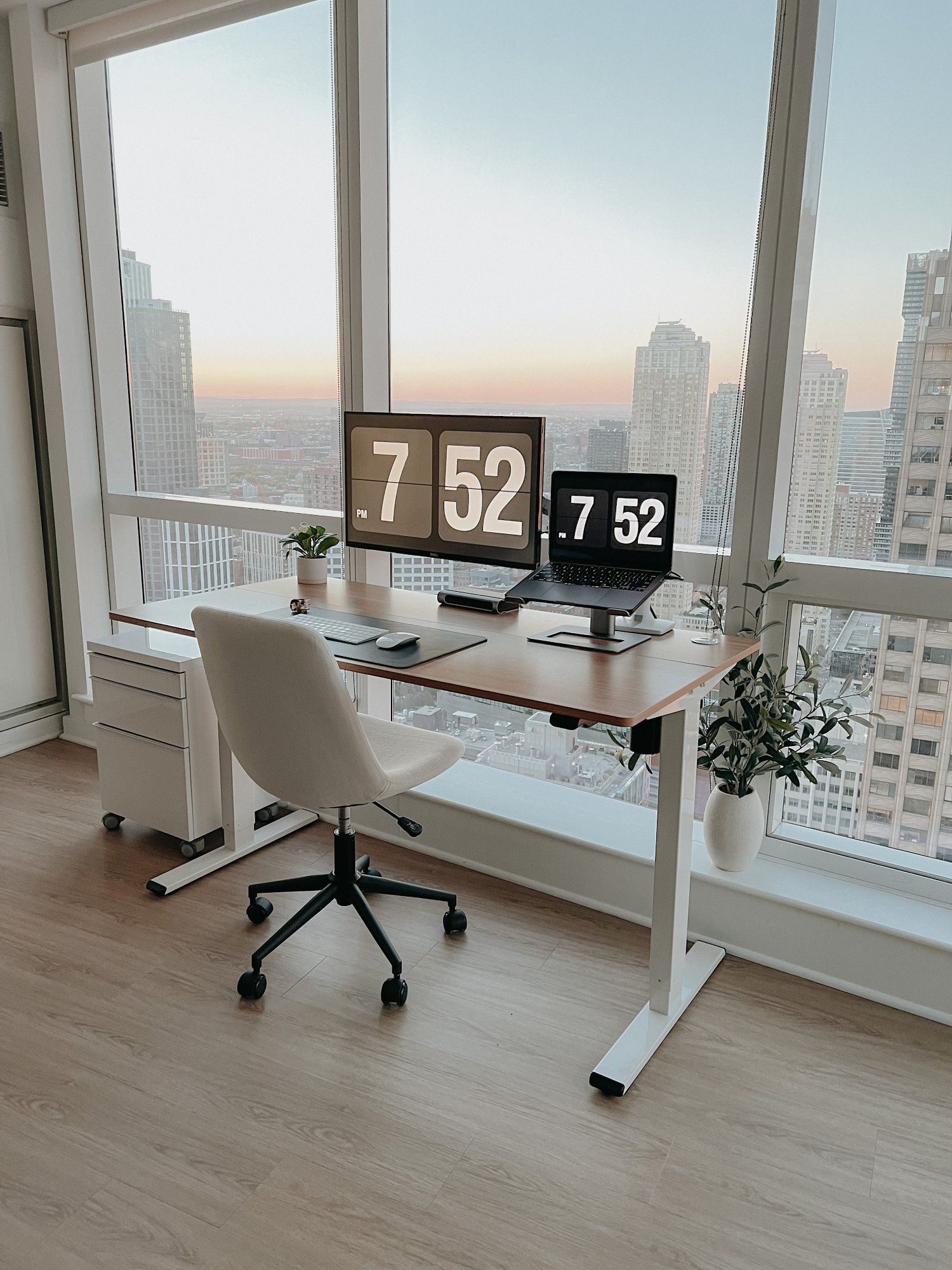 A minimalist home office setup with an expansive city view, featuring a sleek white desk, ergonomic chair, laptop, and a potted plant