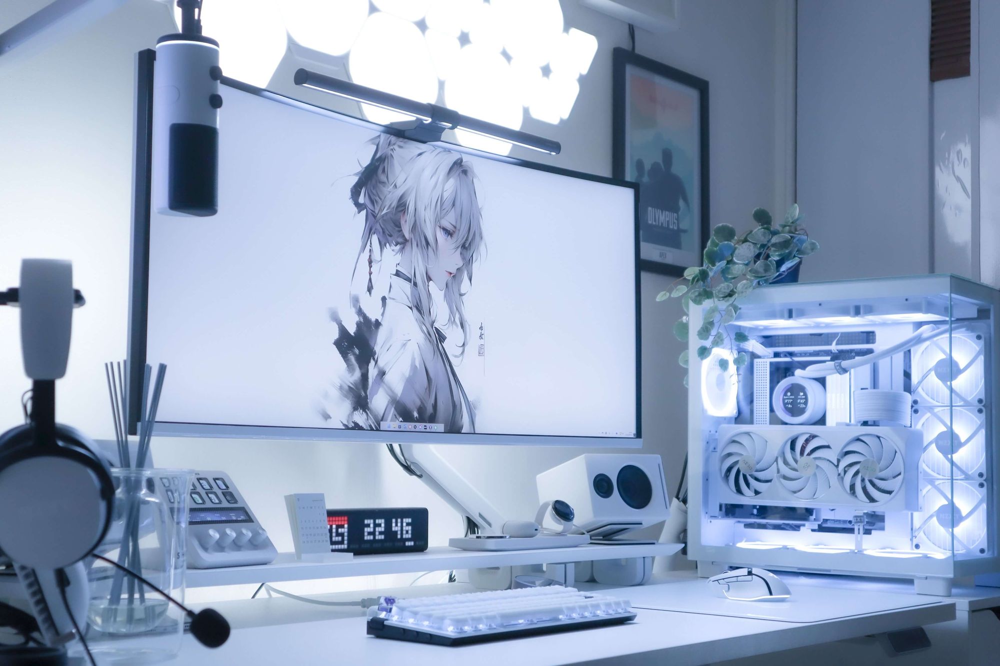 A stylish and futuristic gaming desk setup featuring a large monitor with an anime character wallpaper, backlit by ambient lighting, a custom white PC case with internal lighting, modern peripherals, and a digital clock, all arranged neatly on a clean white desk