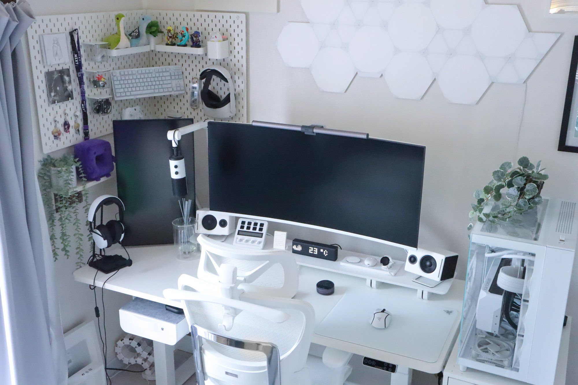 A chic and contemporary workstation with a large ultrawide monitor, white ergonomic chair, and a matching white desk housing an organised array of gadgets including speakers, a temperature display, and a gaming mouse