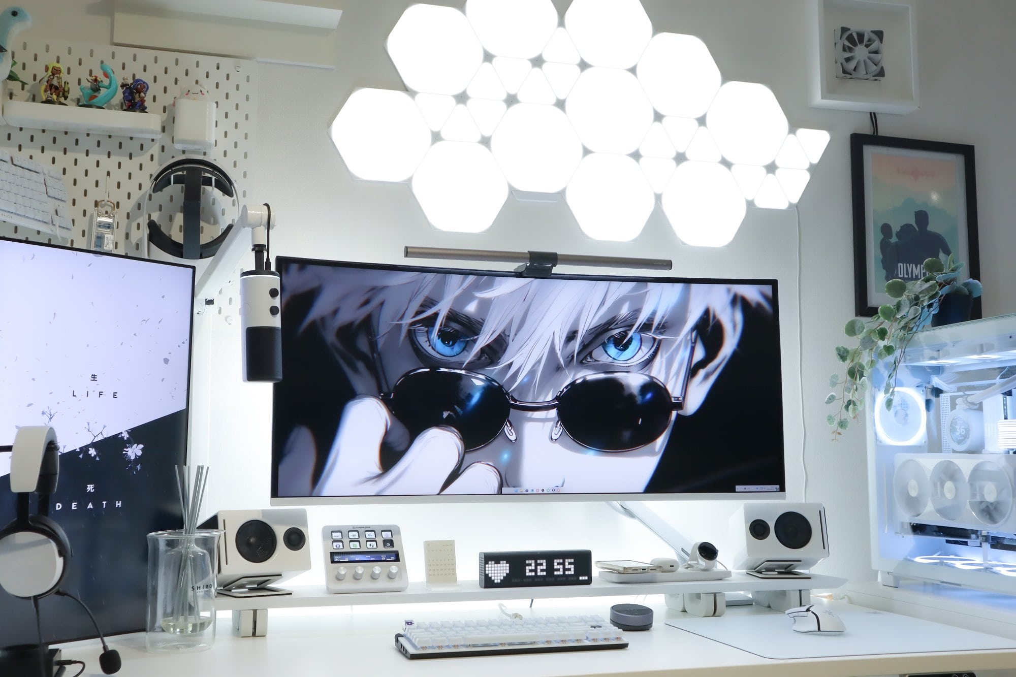 A modern desk setup with an anime-themed ultrawide monitor, flanked by speakers and tech accessories, with an LED-lit custom PC on the right, all under a striking ceiling light fixture