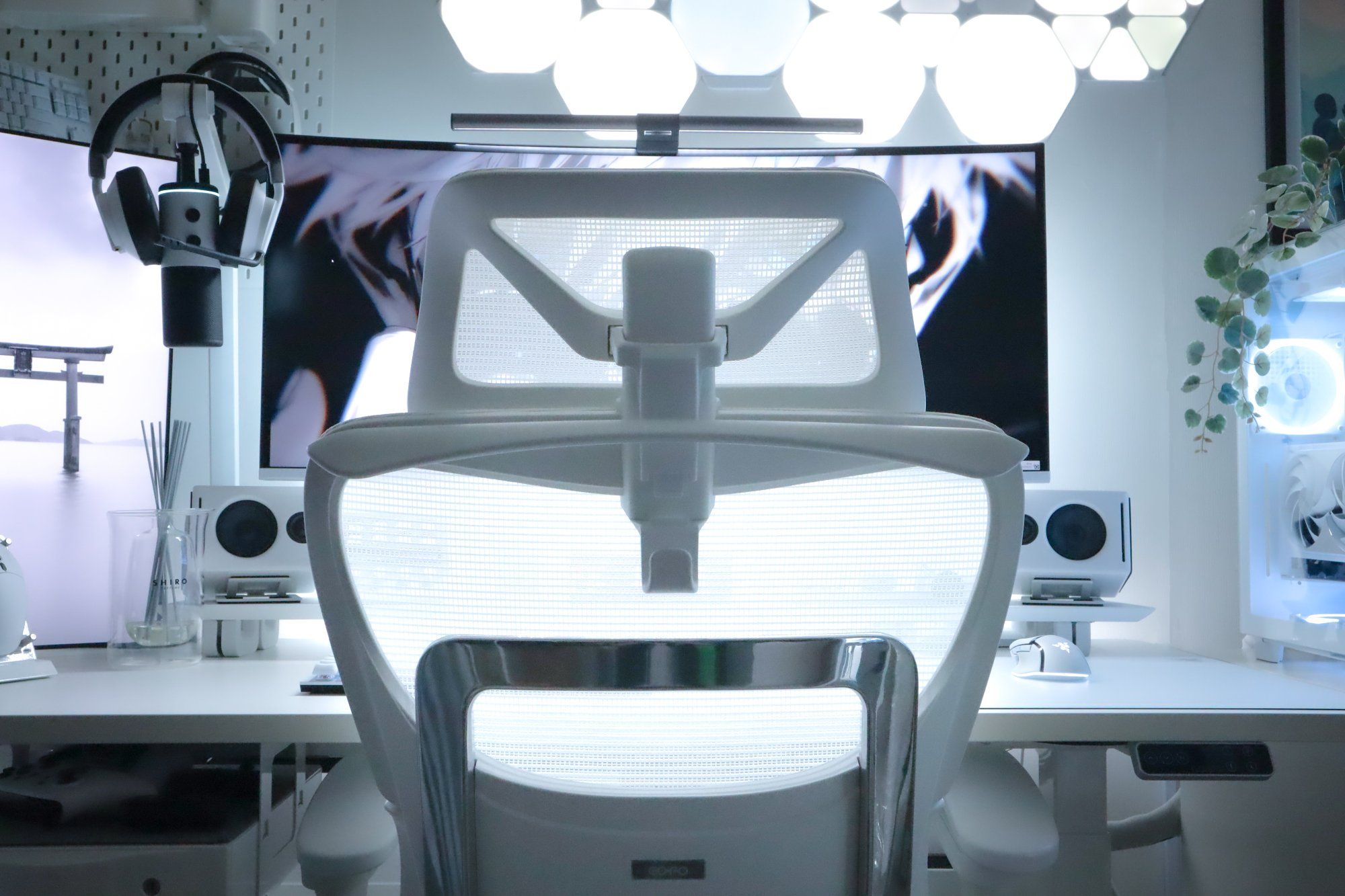 An ergonomic mesh office chair in a stylish white workspace, facing an ultrawide monitor with anime artwork, complemented by modern desk accessories, ambient lighting, and a contemporary PC setup