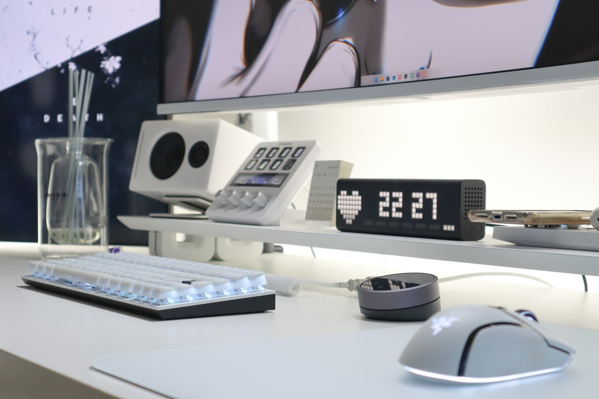 A close-up of a modern desk setup, highlighting a mechanical keyboard with backlit keys, a high-precision gaming mouse, stereo speakers, and a digital clock displaying the time, all arranged on a clean white desk