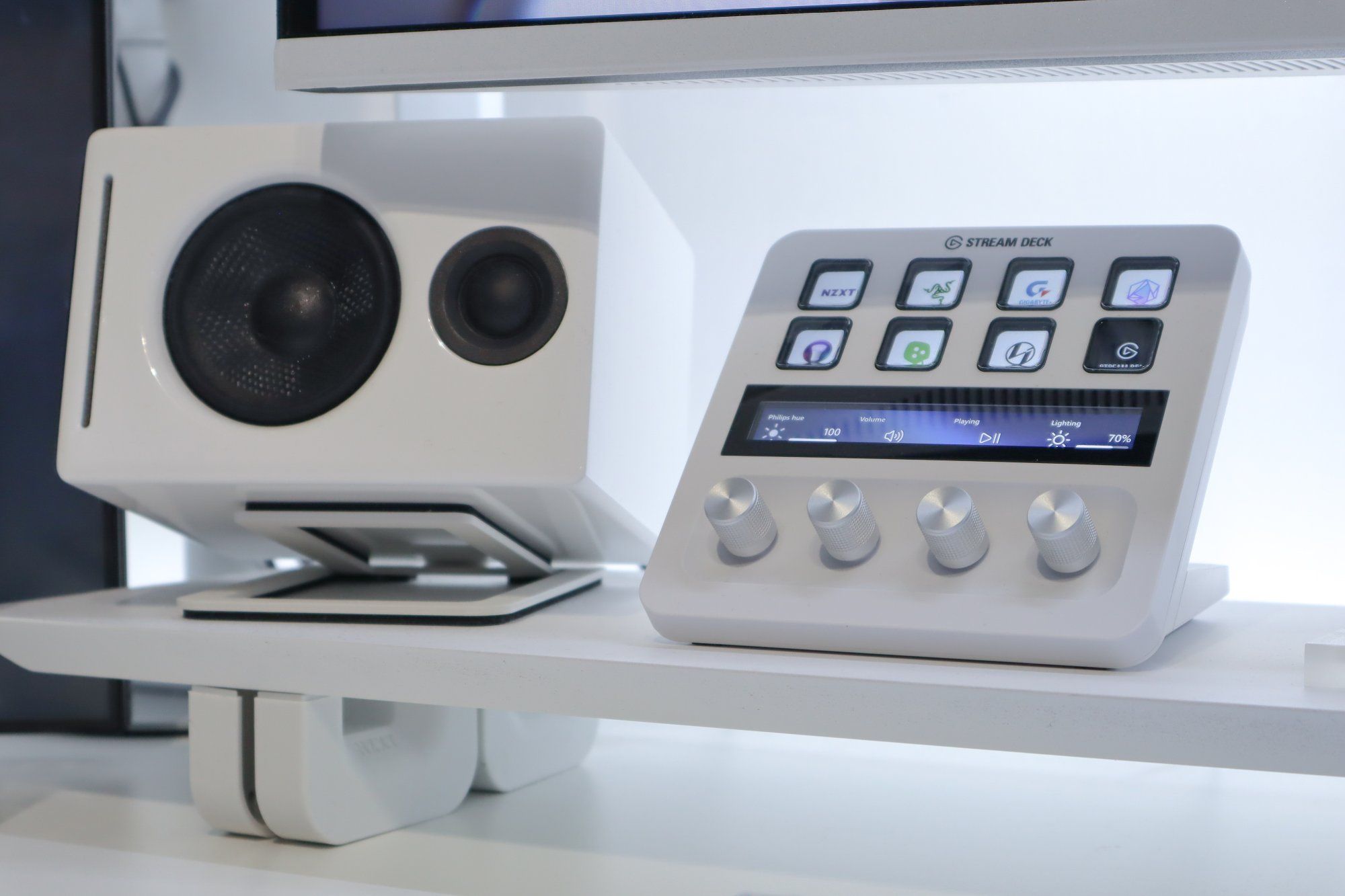 A close-up of a modern desk setup featuring a white stream deck with customisable buttons next to a stylish white speaker, part of a high-tech and minimalist workstation