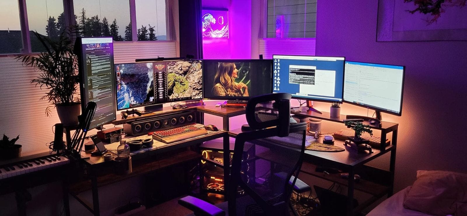 A multi-monitor gaming and work setup in a room at dusk, with ambient purple lighting