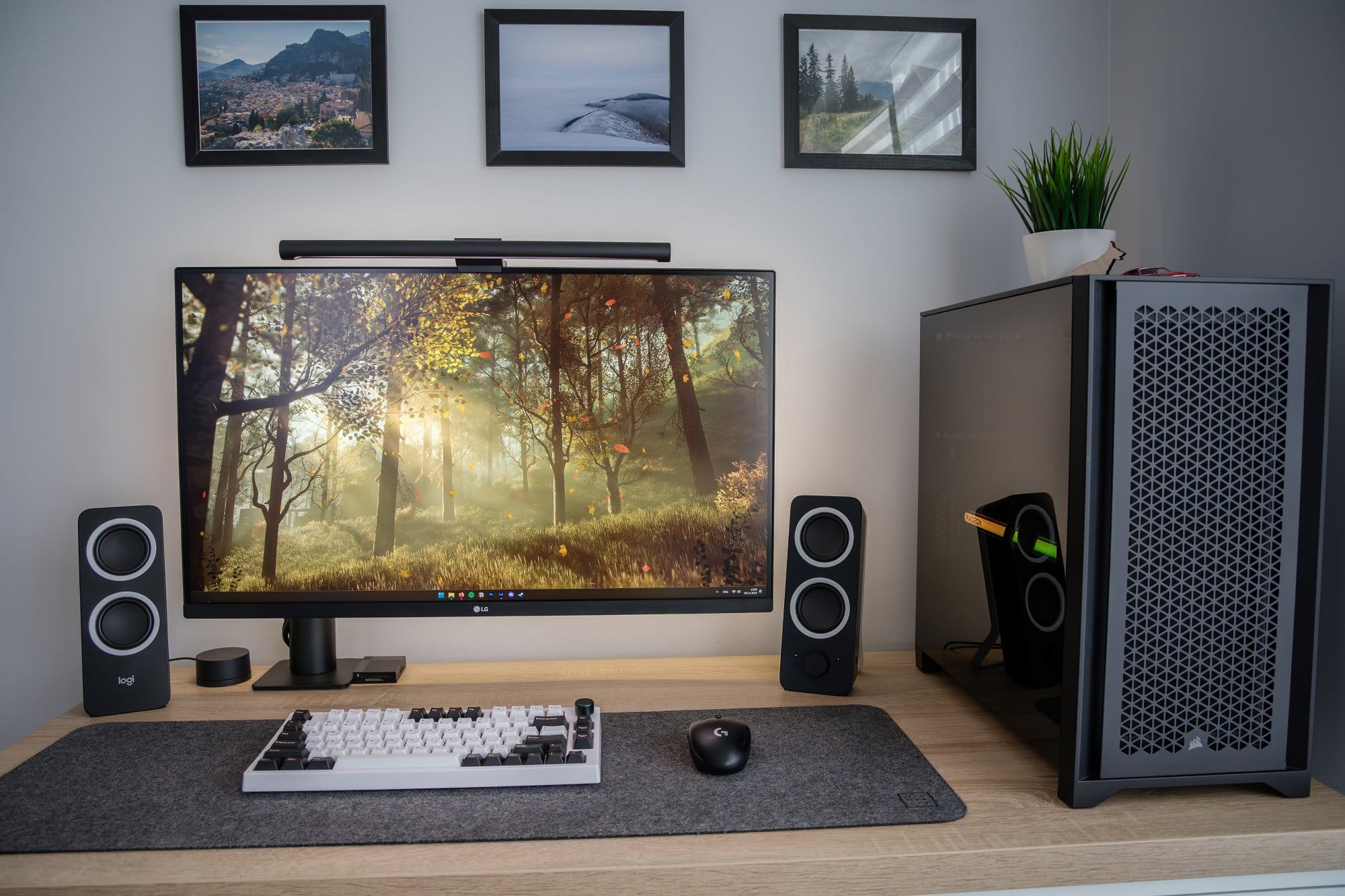 A close-up view of a well-organised desk with a mechanical keyboard and ergonomic mouse, flanked by stereo speakers, next to a high-end computer tower and a monitor displaying an autumnal forest scene