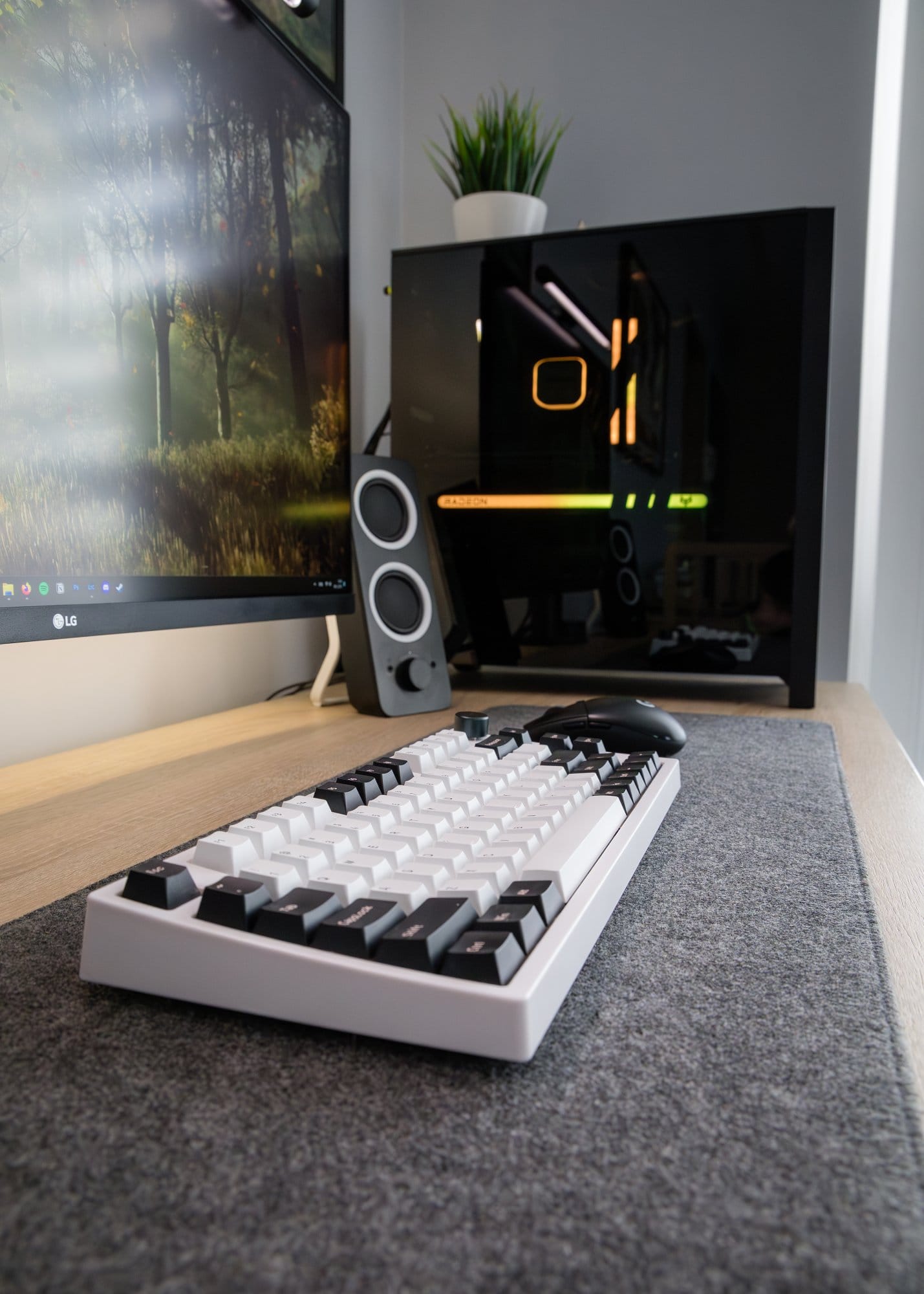 A focused view on an Epomaker mechanical keyboard with white keys on a desk mat, with a gaming mouse to the side, and in the background, a monitor and a high-end PC tower with LED lighting