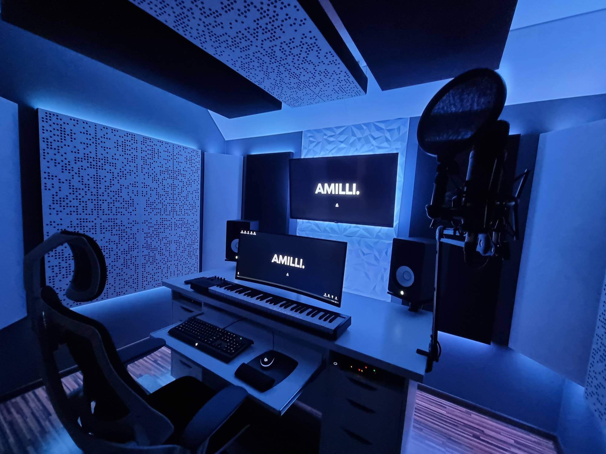 A modern music production setup illuminated by blue light, featuring a keyboard, computer monitors, studio speakers, and a professional microphone in an acoustically treated room