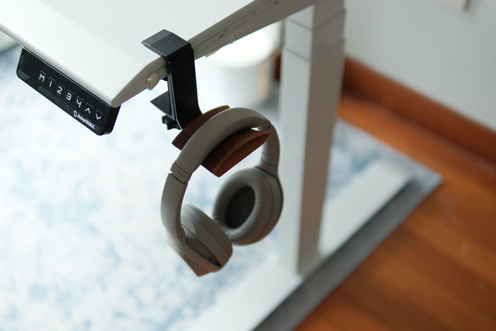 A pair of over-ear headphones hanging on a hook attached to a white standing desk