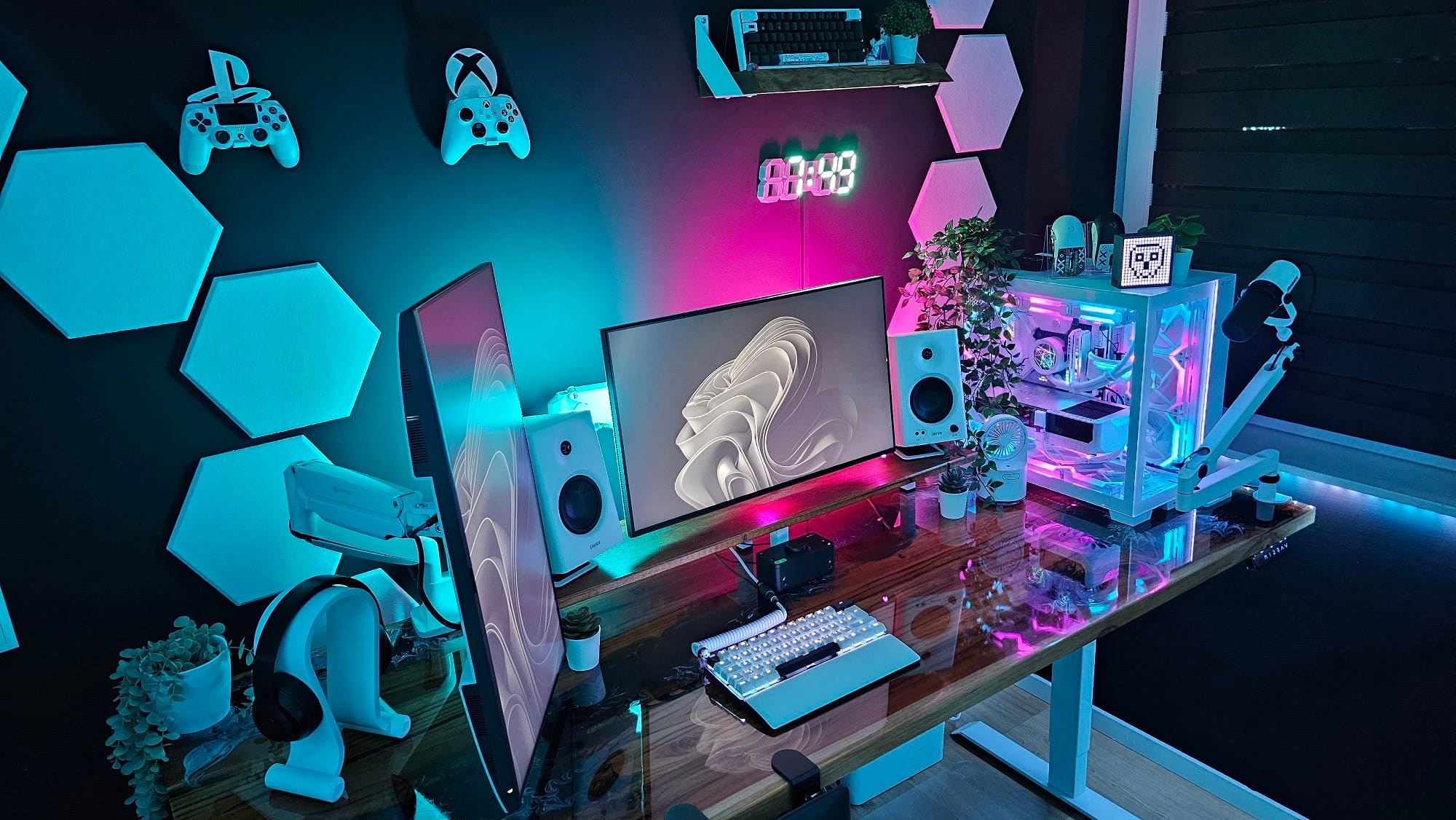 A vibrant gaming setup with neon lighting, featuring a dual monitor configuration, a white mechanical keyboard, a custom-built PC with RGB lighting, speakers, gaming controllers, and a digital clock on a dark wall adorned with geometric panels