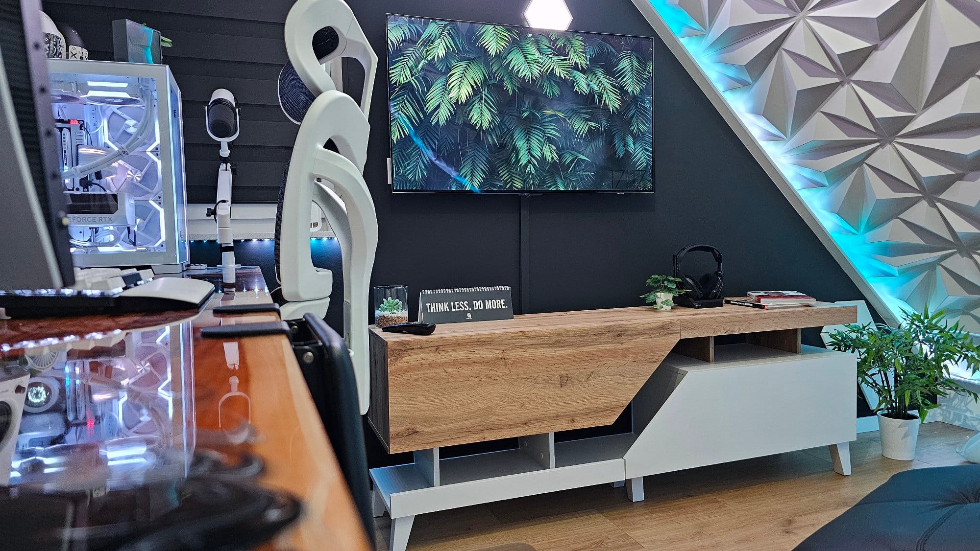 A corner view of a contemporary home office, showcasing a sleek wooden desk with a motivational desk plaque, ambient-lit geometric wall panels, and a mounted TV with a nature-themed display
