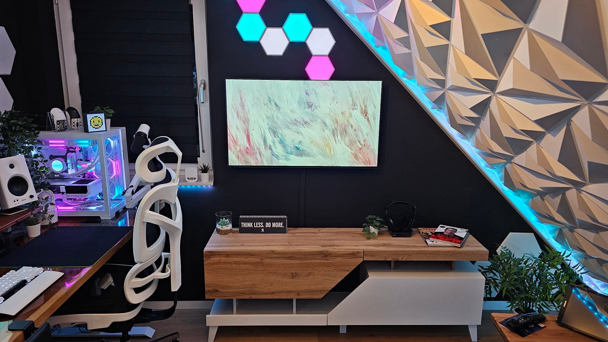 A sleek home office setup with an abstract painting on the wall, an illuminated geometric panel, a white ergonomic chair, and a wooden desk with a motivational sign, surrounded by ambient lighting and modern technology