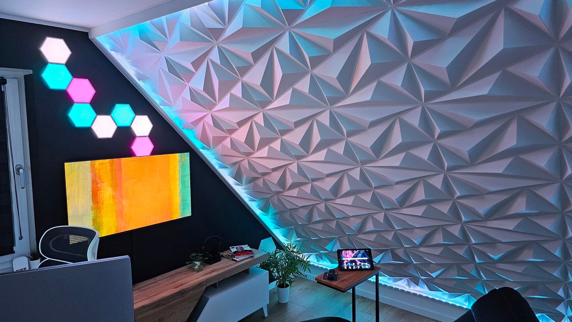A modern home office corner with a geometric 3D wall art installation, illuminated by ambient lighting, a mounted abstract painting, and a tablet on a side table, creating a vibrant and artistic workspace atmosphere