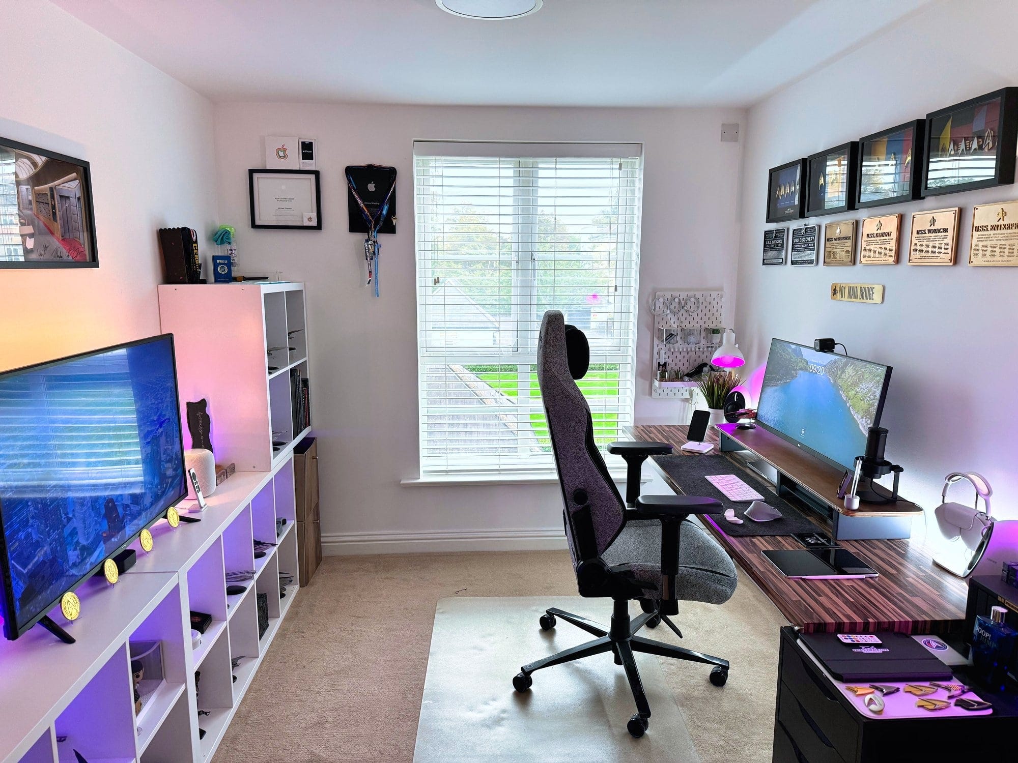 A spacious home office featuring a large window, a desk with an ultrawide monitor, a gaming chair, and shelves with ambient lighting