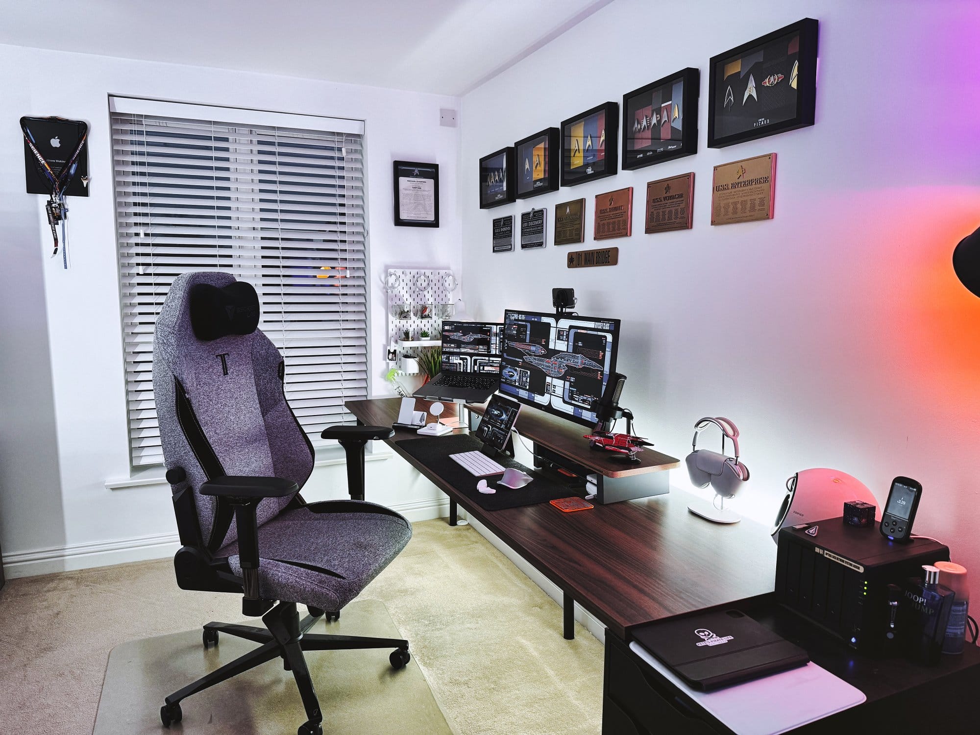 A gaming chair positioned in front of a desk in a home office, backlit with ambient lighting, and adorned with Star Trek collectibles and professional certificates on the wall