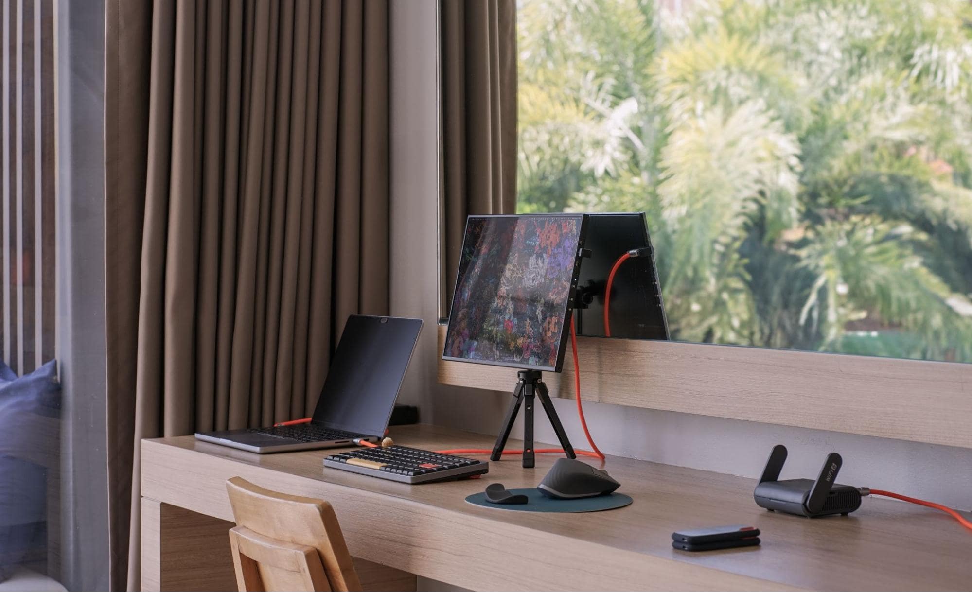 A sleek portable desk setup in Tokyo with a laptop, a tablet displaying colourful graphics on a tripod stand, and a mechanical keyboard