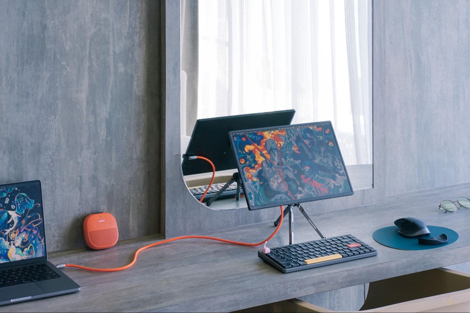 A minimalist desk setup in Tokyo with a laptop, a tablet on a stand, a mechanical keyboard, and a portable speaker, all connected by a striking orange cable