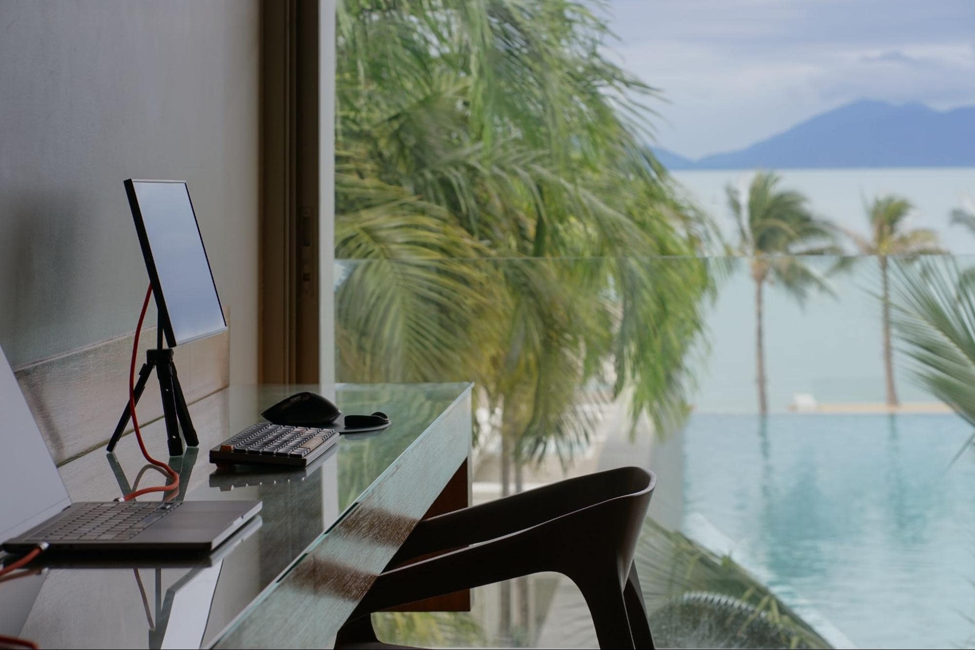 A tranquil workspace featuring a tablet on a stand and a keyboard with a stunning ocean view and palm trees in the background, offering a peaceful setting for focus and inspiration