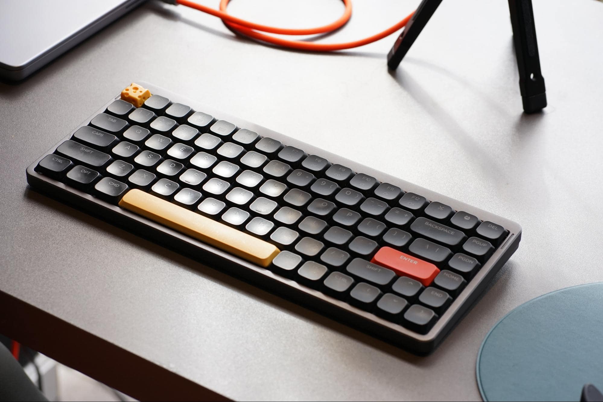 A close-up of a stylish mechanical keyboard with round keys and a distinctive yellow spacebar and red enter key, placed on a modern desk setup