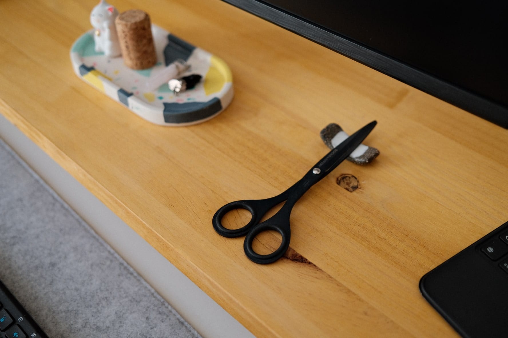  A close-up of a wooden desk with a pair of black scissors, a cork stopper, and a decorative tray with a small figurine