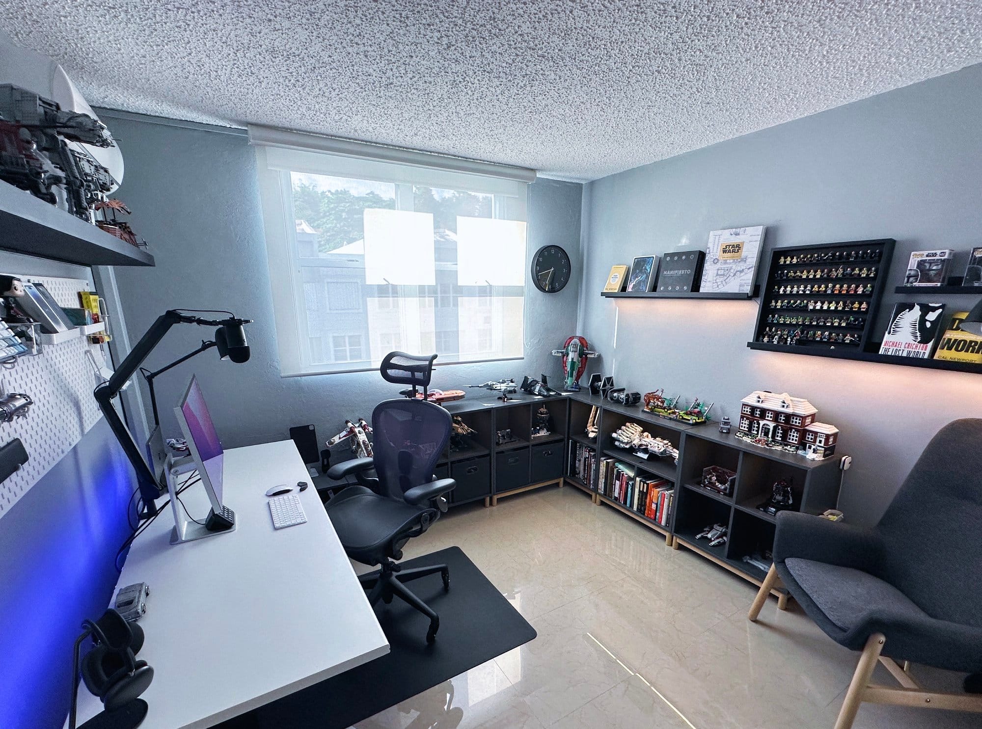  An organised office room with a desk, ergonomic chair, computer setup, shelves with books and collectibles, and decorative wall art