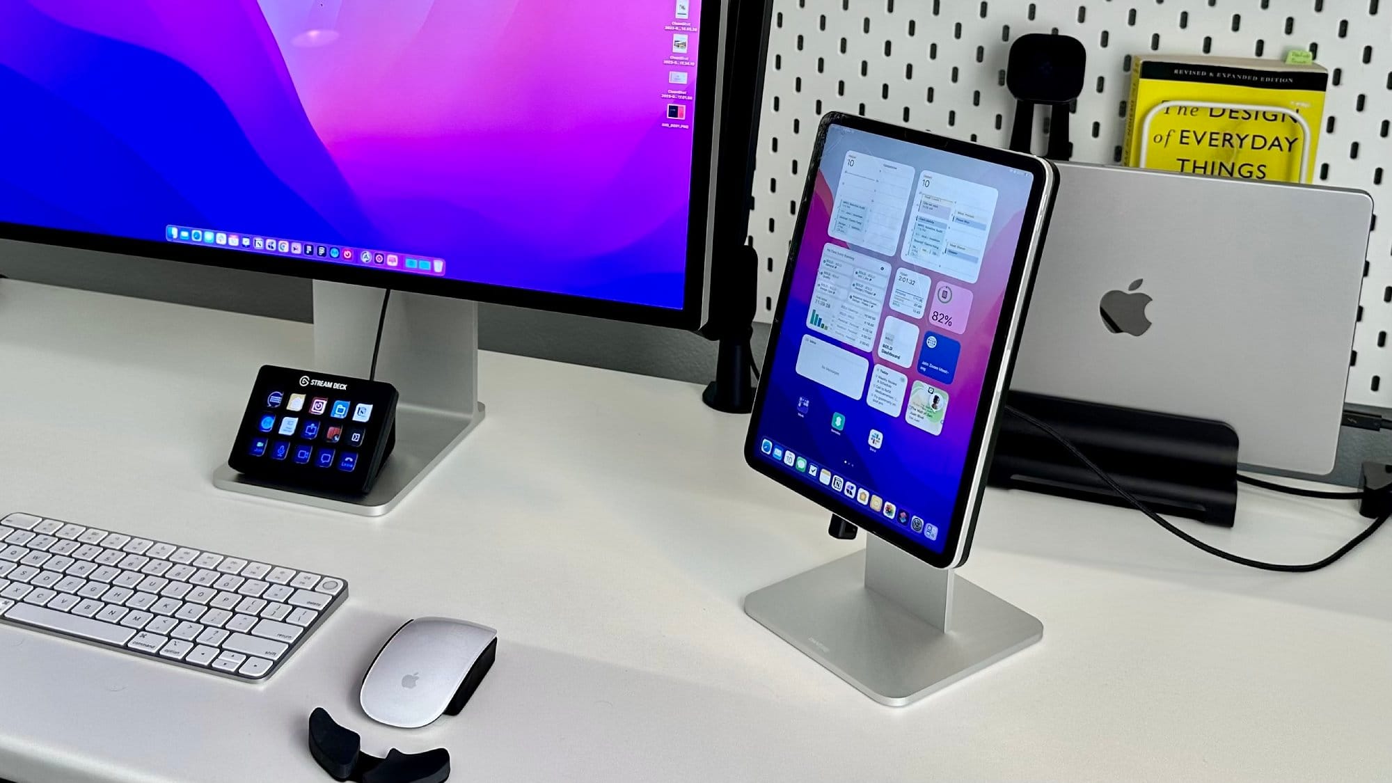  A modern workspace with two monitors, a keyboard, a mouse, a tablet, a smartphone on a stand, and a book titled The Design of Everyday Things in the background