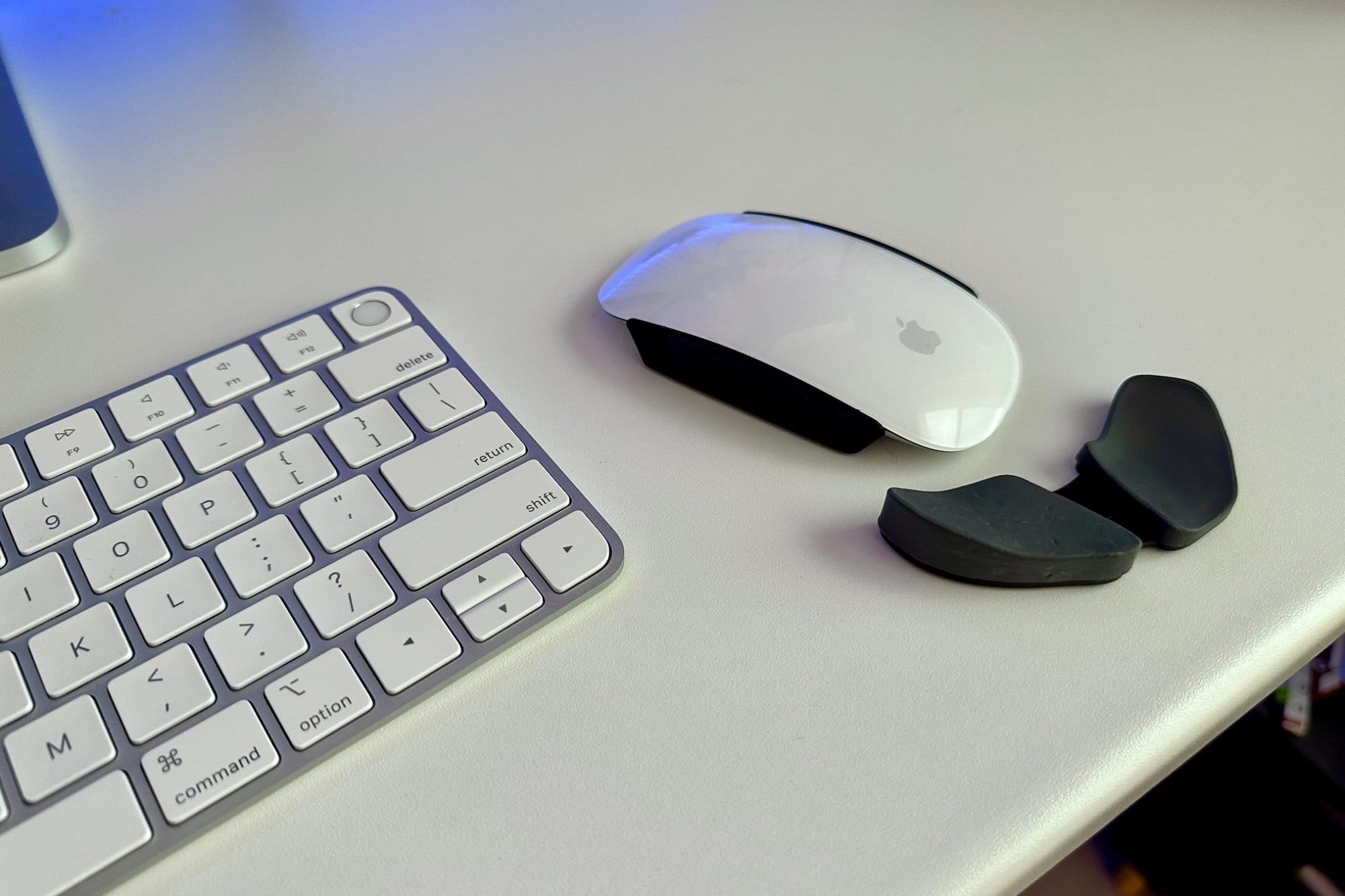 A close-up of a white desk with a wireless keyboard, a magic mouse, and a black Deltahub wrist rest