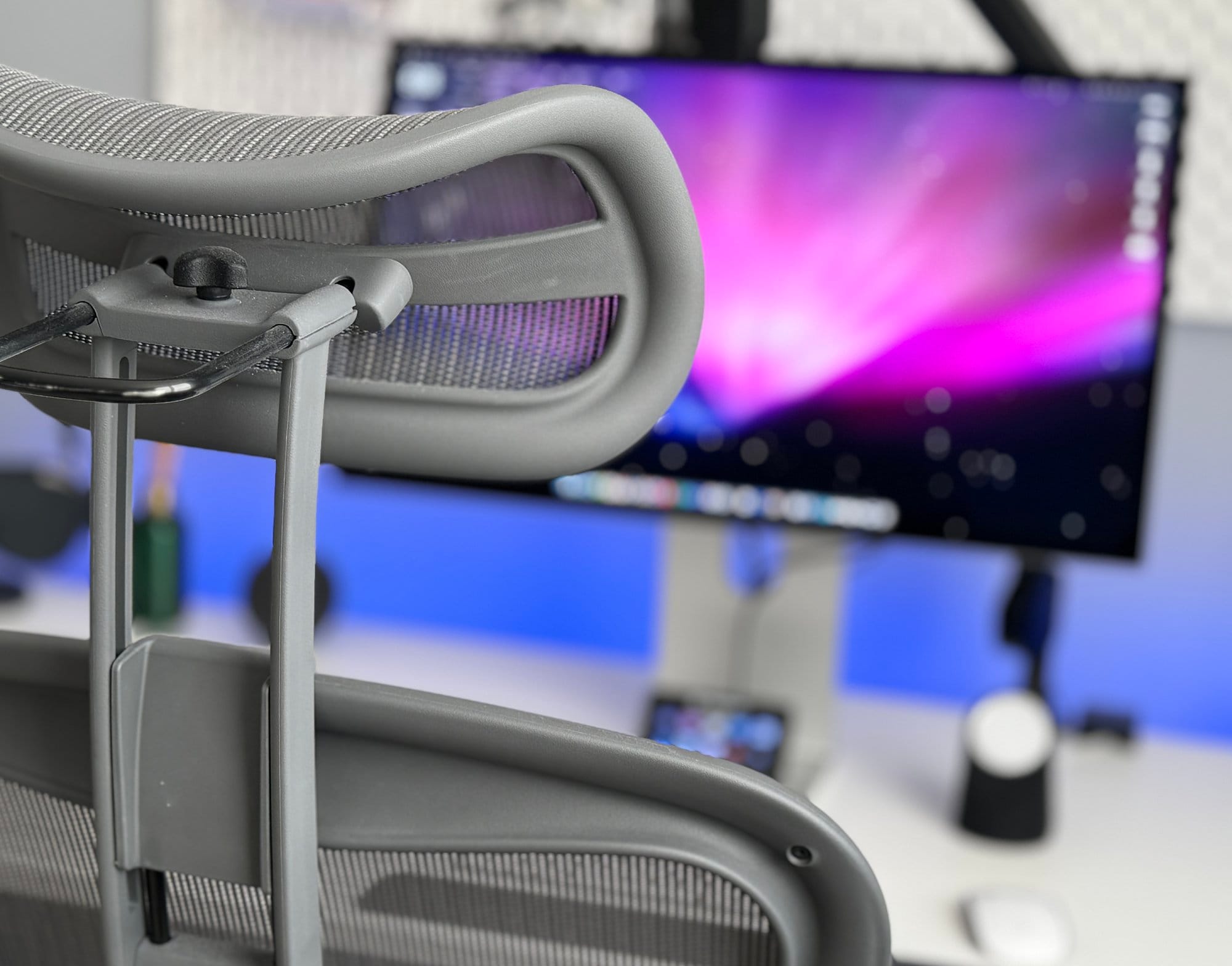  A close-up view of an ergonomic office chair with a focus on the armrest, overlooking a desk with a monitor, keyboard, and a speaker, all in a modern workspace setting