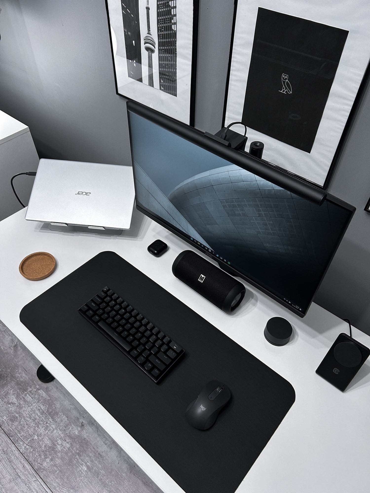 An overhead view of a minimalist desk with a laptop, curved monitor, keyboard, mouse, and framed art on the wall