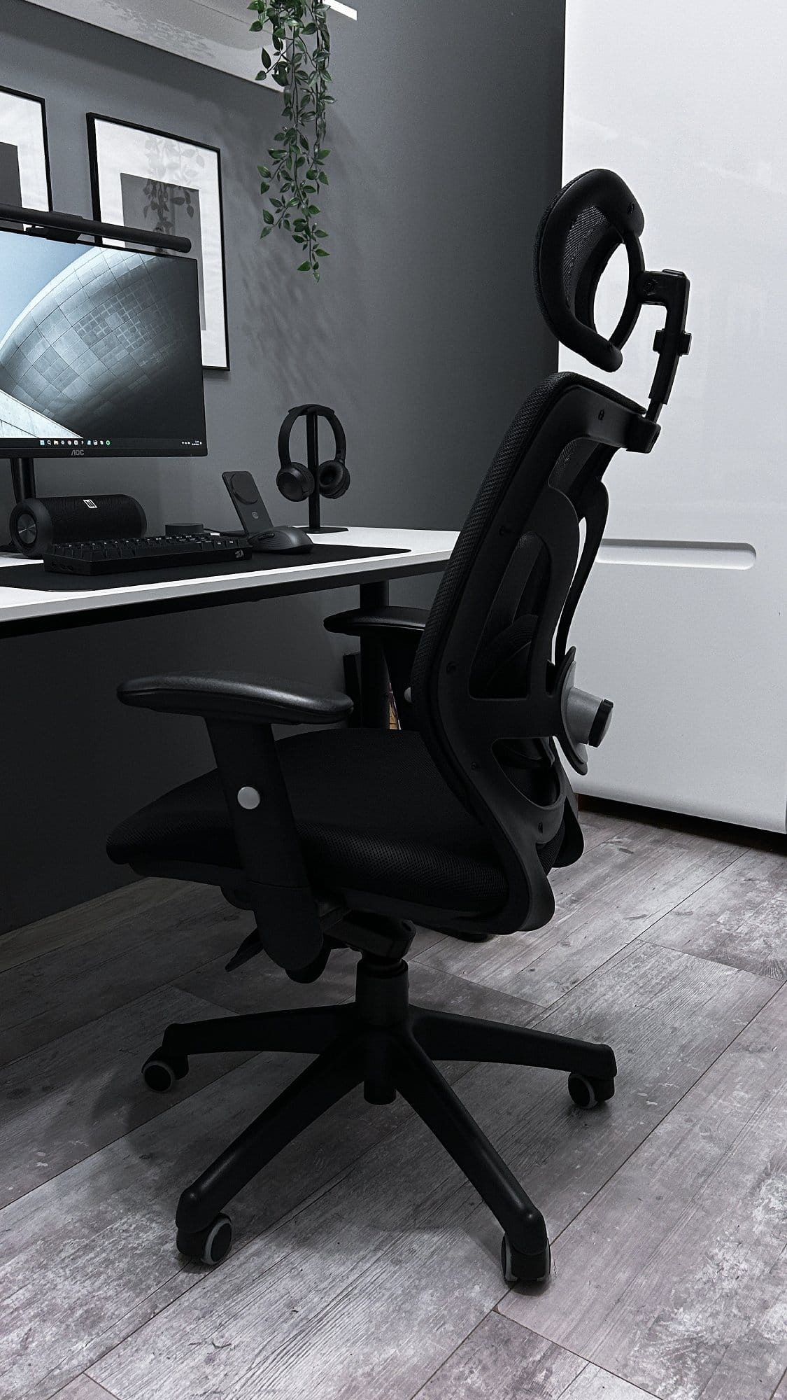 A black ergonomic office chair in the foreground with a modern desk and computer setup in the background
