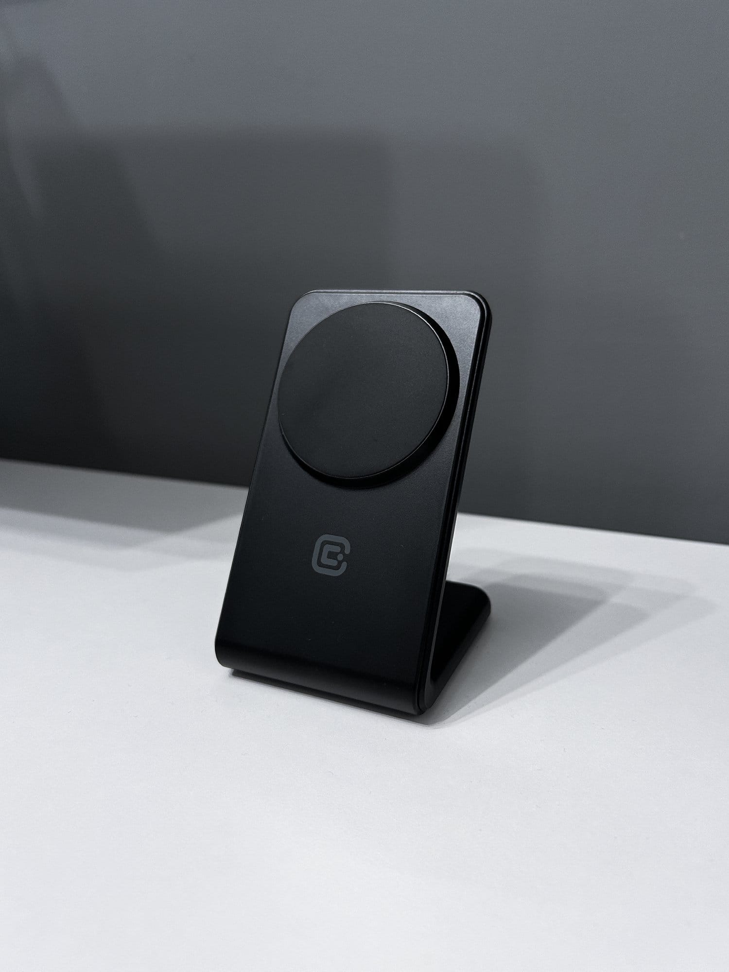 A black wireless charging stand on a white table against a dark grey wall