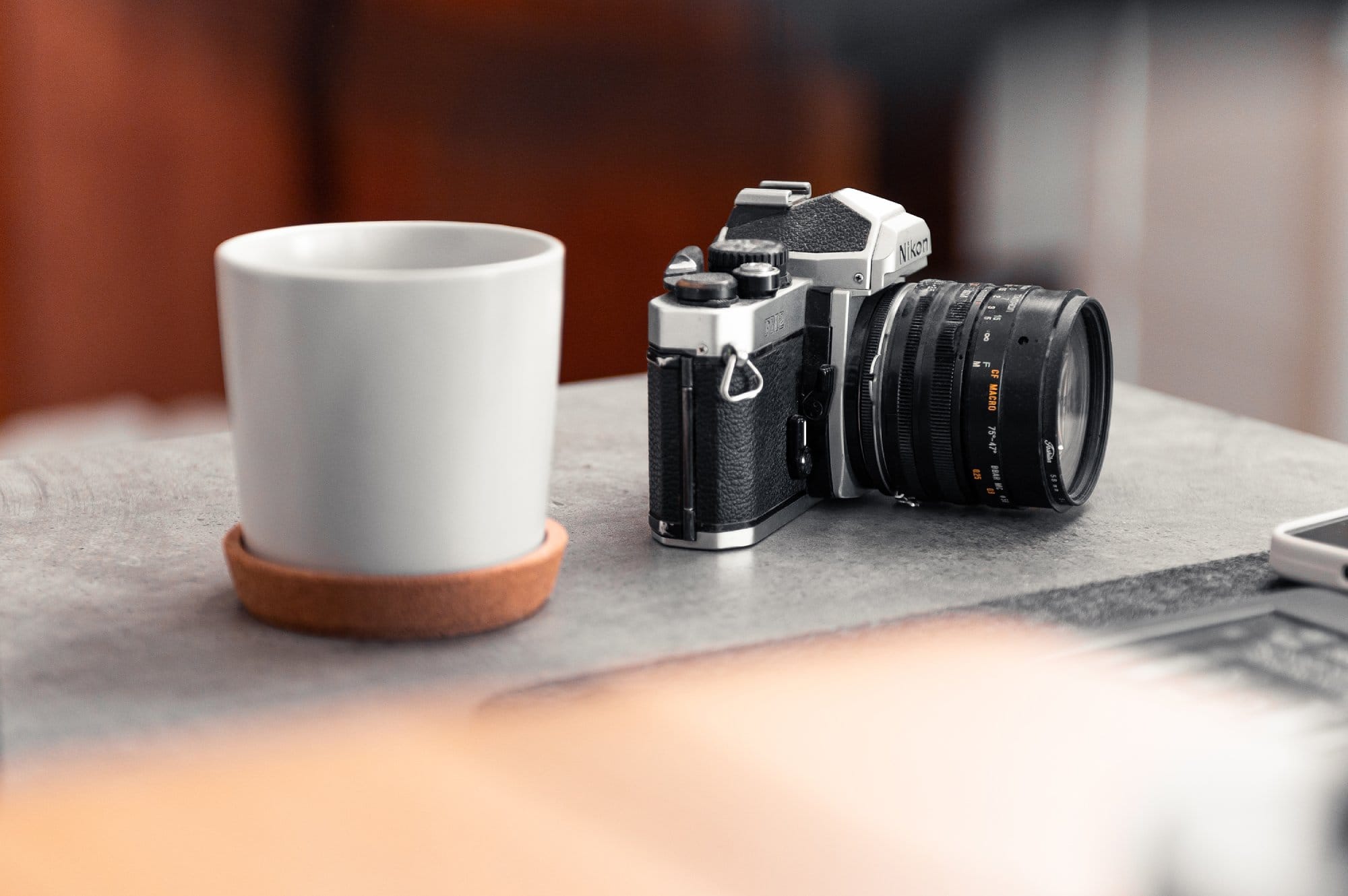A vintage Nikon FM2 camera placed on a desk next to a white mug on a coaster