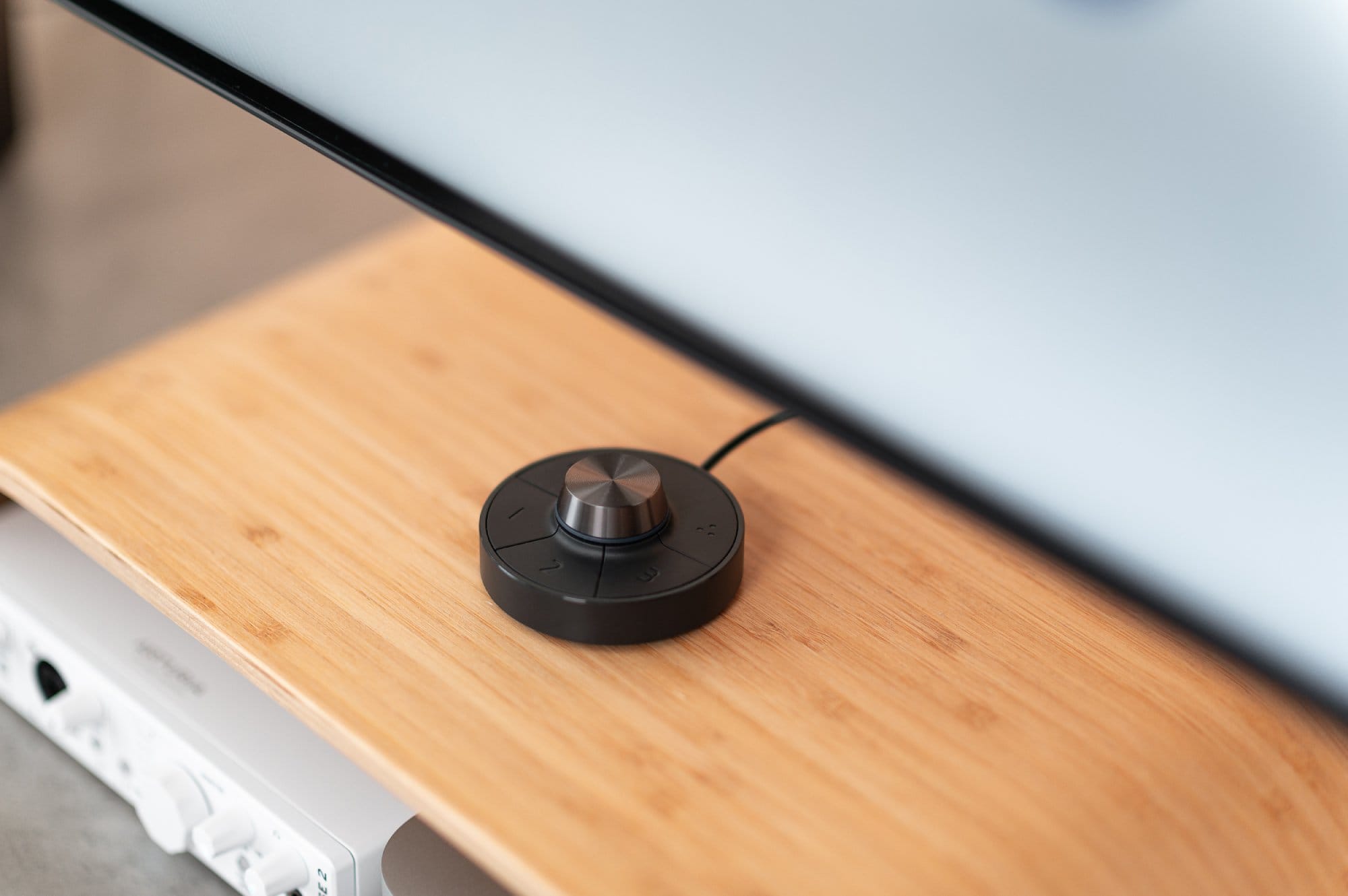 A close-up view of a wooden monitor stand with a black dial controller for a monitor