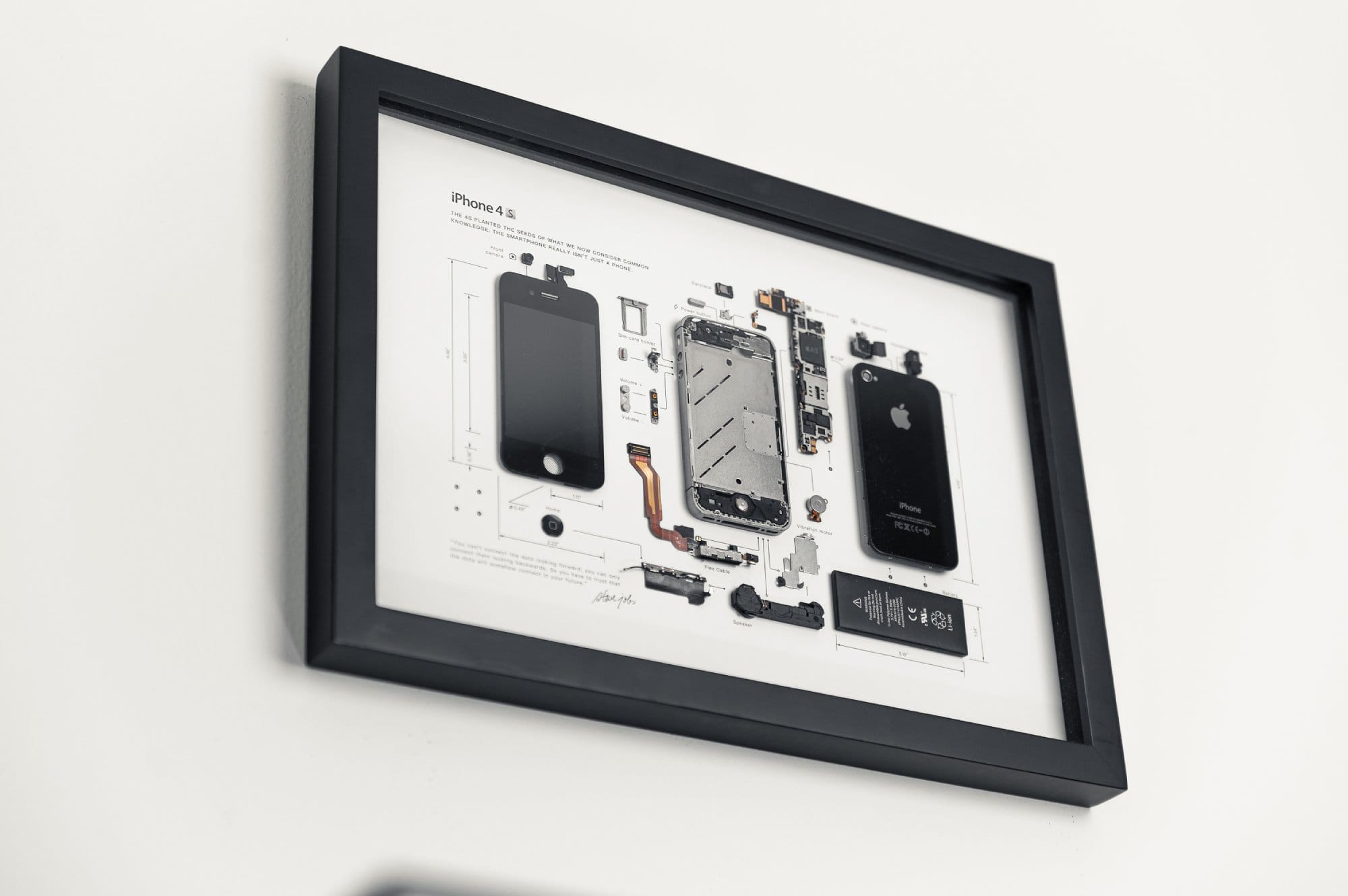 A framed schematic diagram of an iPhone 4s, displaying its disassembled parts, mounted on a white wall