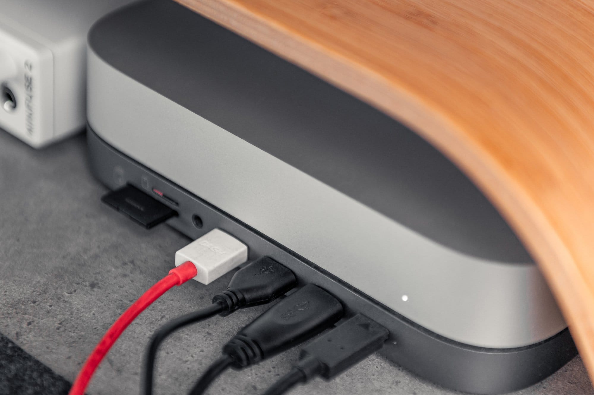  A close-up of a desk showing the underside of a wooden monitor stand with a laptop dock underneath and various cables plugged into it, including a prominent red one