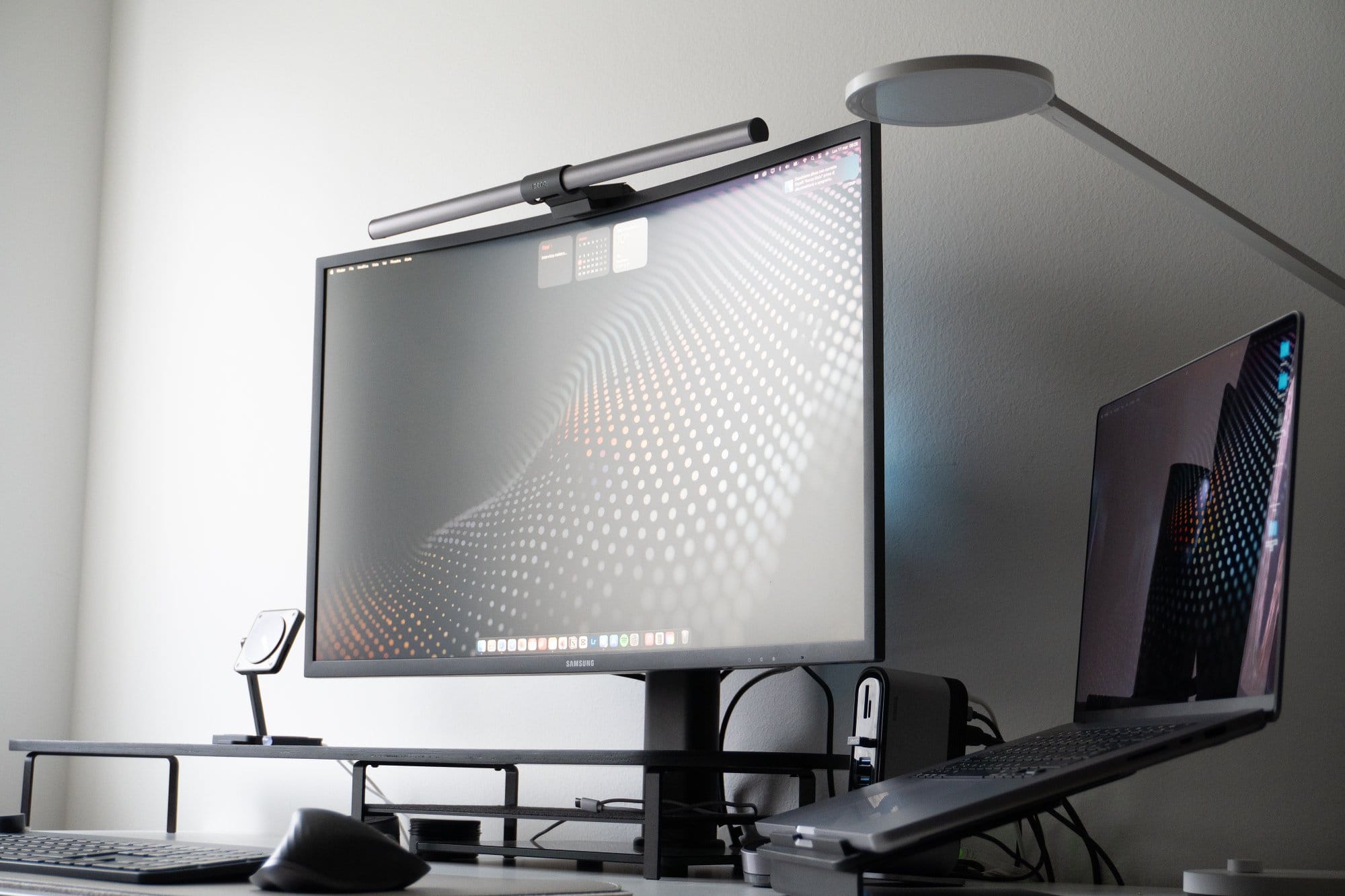 A modern workspace with a large monitor and a laptop on a stand