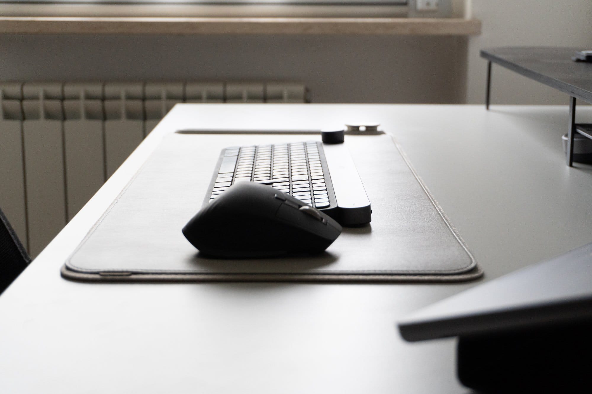 An ergonomic mouse and keyboard on a grey mat on a white desk, with a blurred background