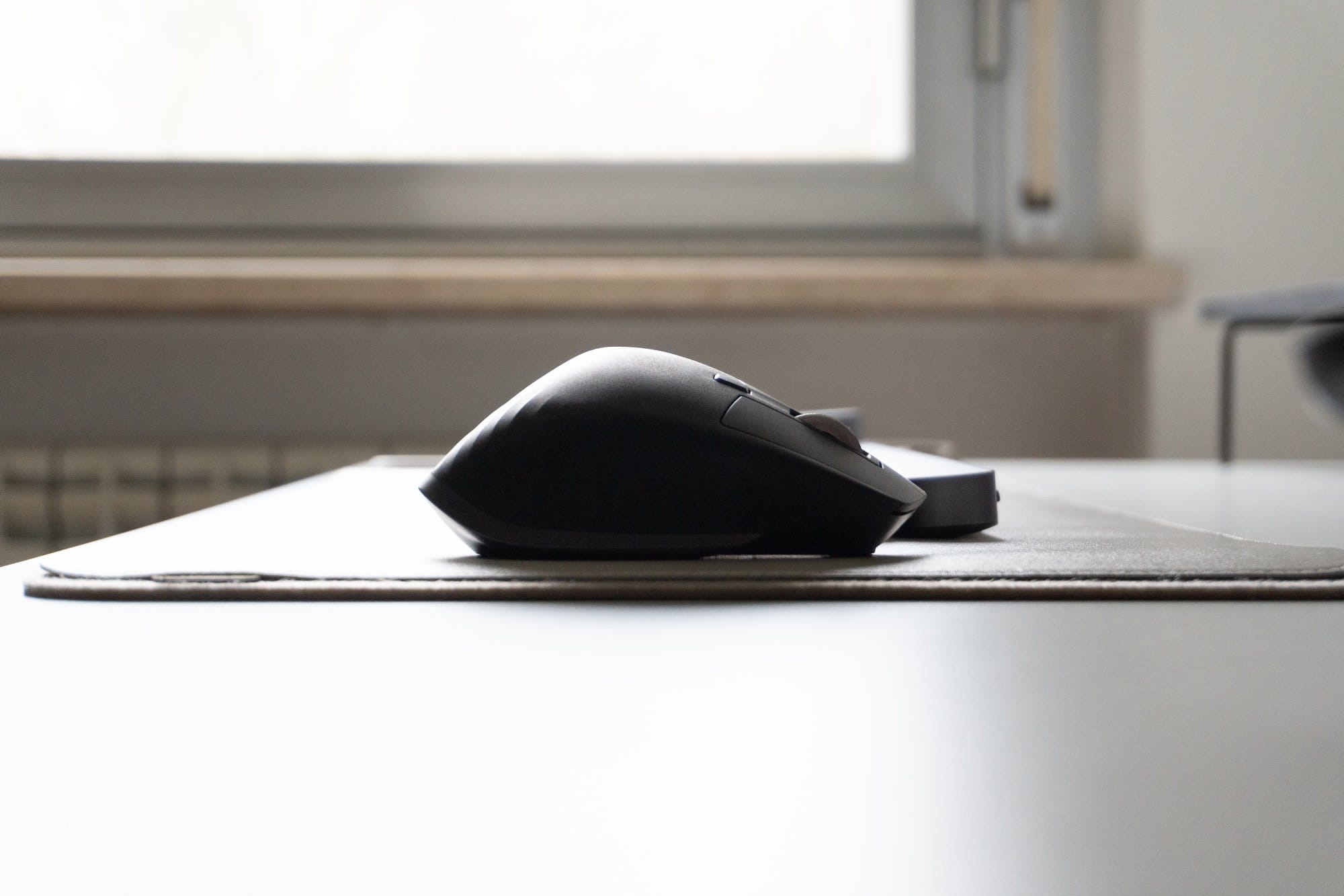 An ergonomic computer mouse on a grey mat placed on a white desk, with a soft-focus background