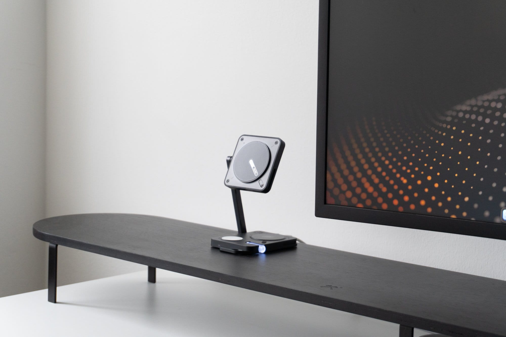 A minimalist desk setup featuring a black shelf with a metallic mobile phone stand and a portion of a monitor to the right