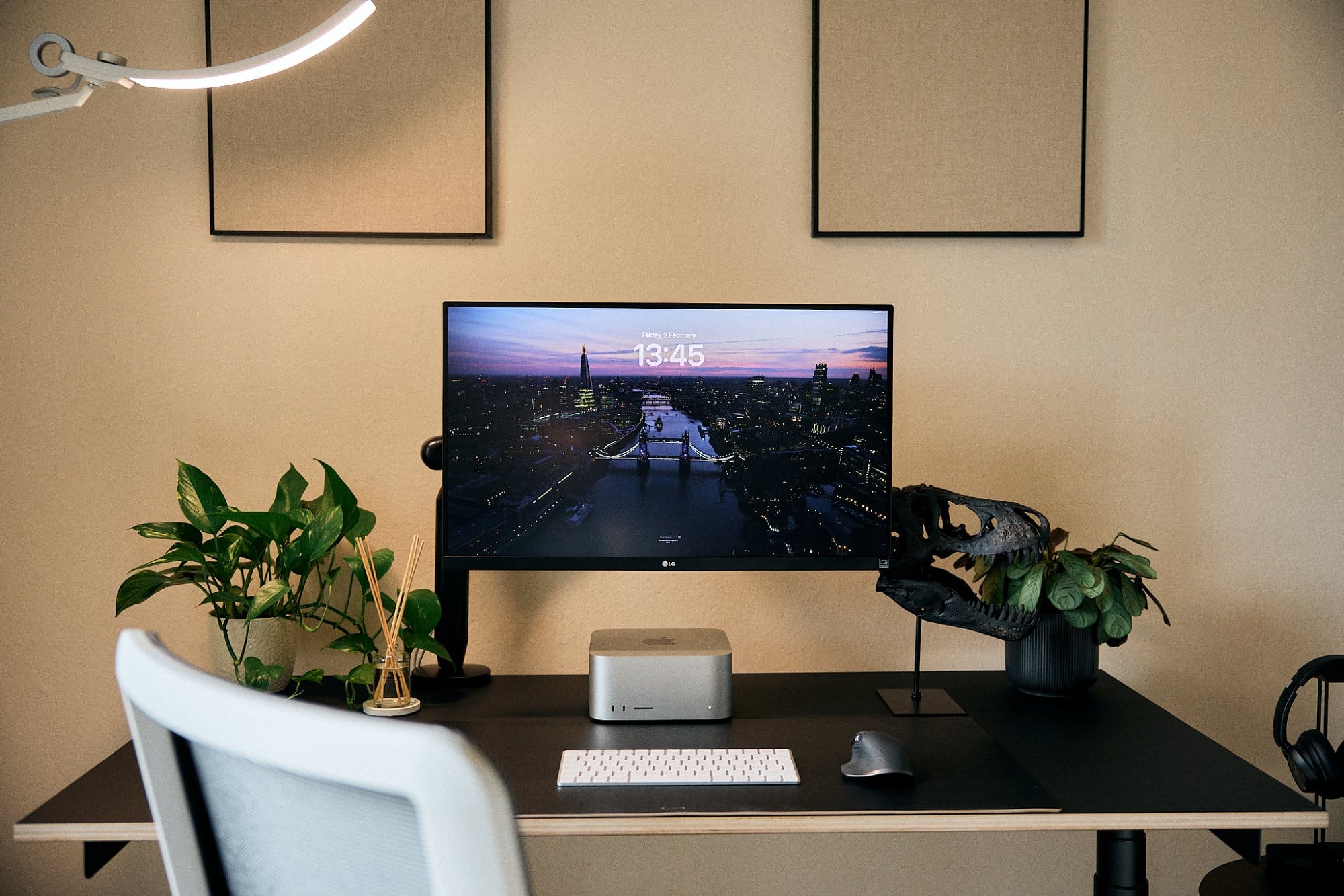 A modern home office setup with a large monitor displaying a cityscape wallpaper, flanked by plants, and accompanied by a keyboard, mouse, desktop computer, and headphones, all against a backdrop of neutral-toned wall art