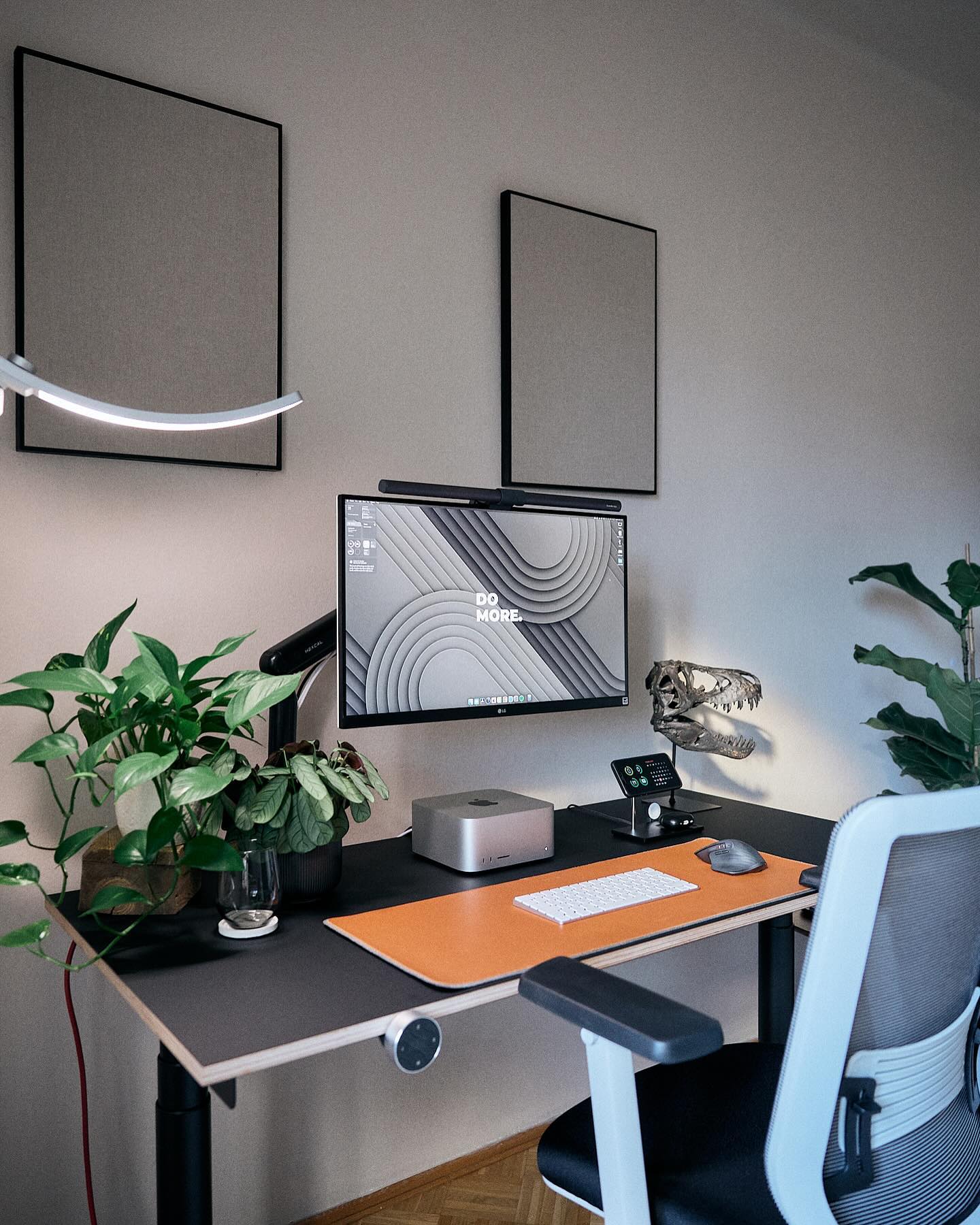 An organised office space with a standing desk, displaying a computer with an inspirational wallpaper, a Mac Studio, a smartphone on a dock, and vibrant desk accessories, complemented by indoor plants and modern wall art