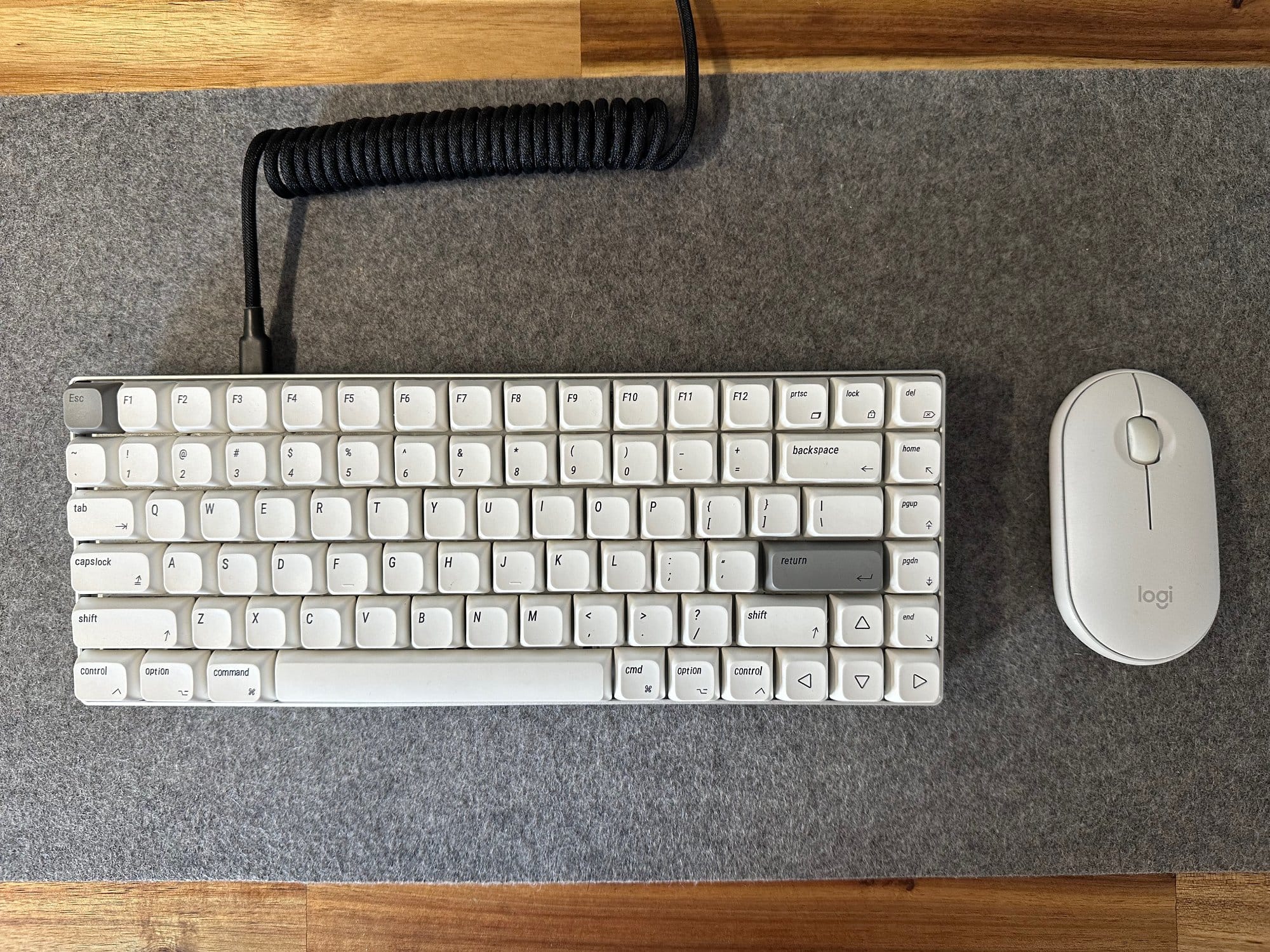 A white mechanical keyboard with a coiled cable next to a white Logitech mouse, both resting on a grey desk mat