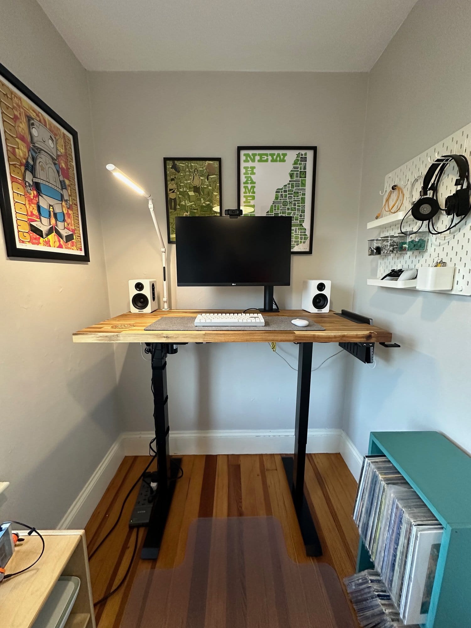 A standing desk with a computer monitor and speakers in a cosy corner, complemented by wall-mounted artwork and an organised pegboard for headphones and supplies
