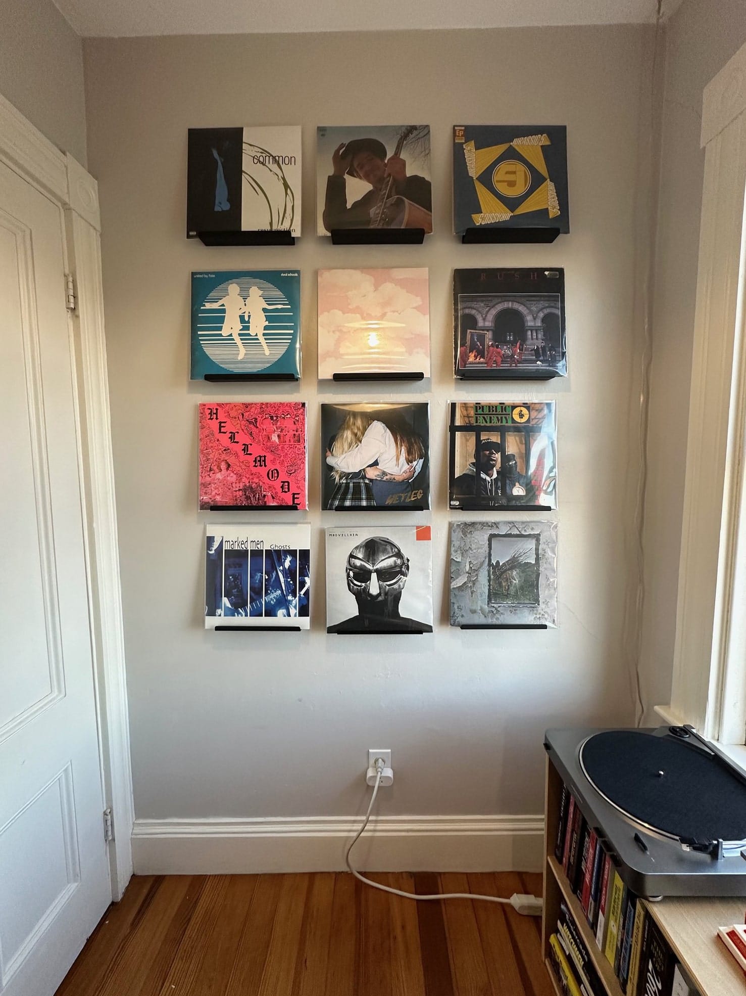A wall decorated with a collection of vinyl record covers displayed in frames, above a hardwood floor and to the side of a record player