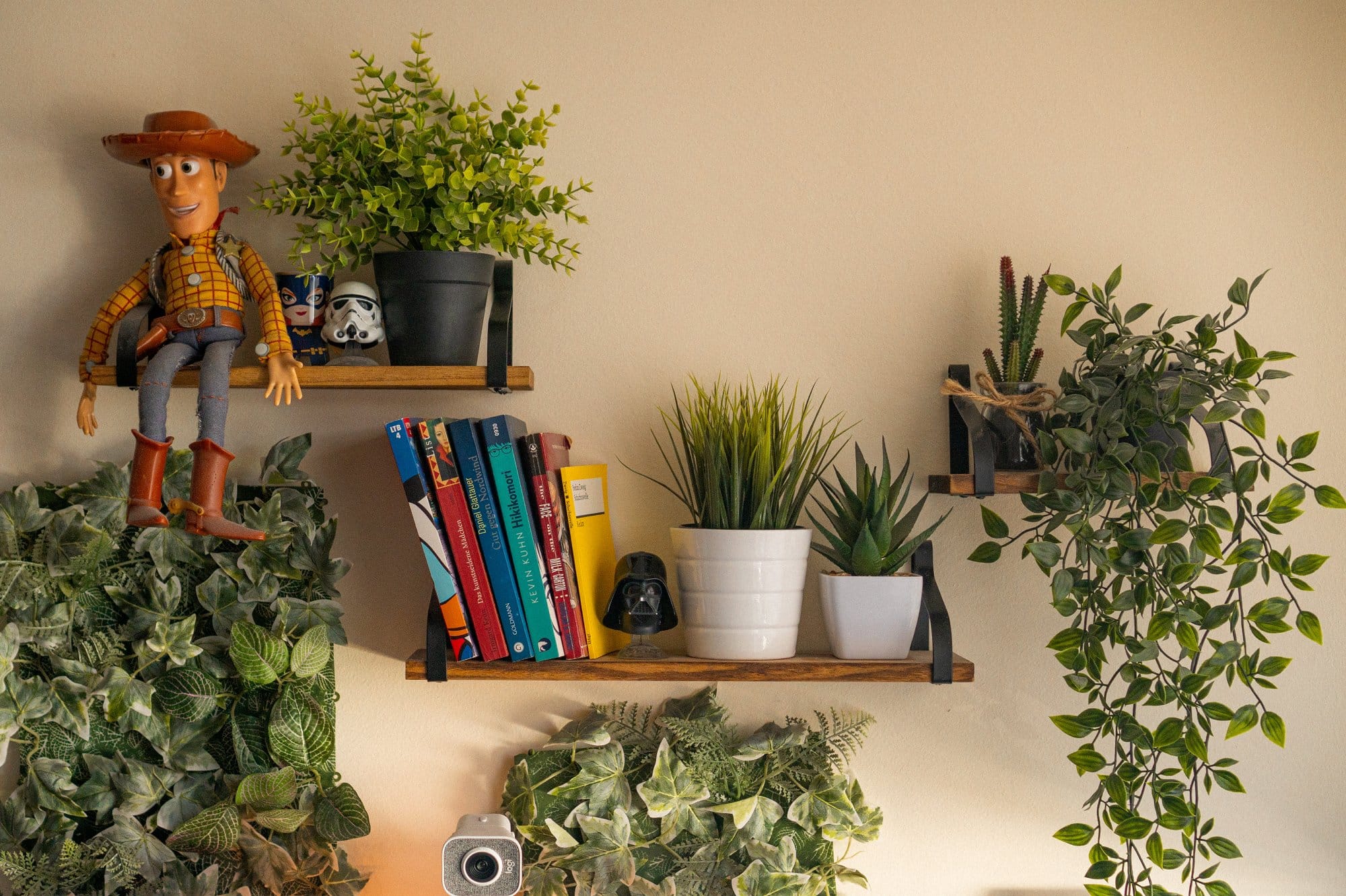 A wall shelf displaying a variety of items including a figurine, books, potted plants, and a camera, creating a lively and decorative corner